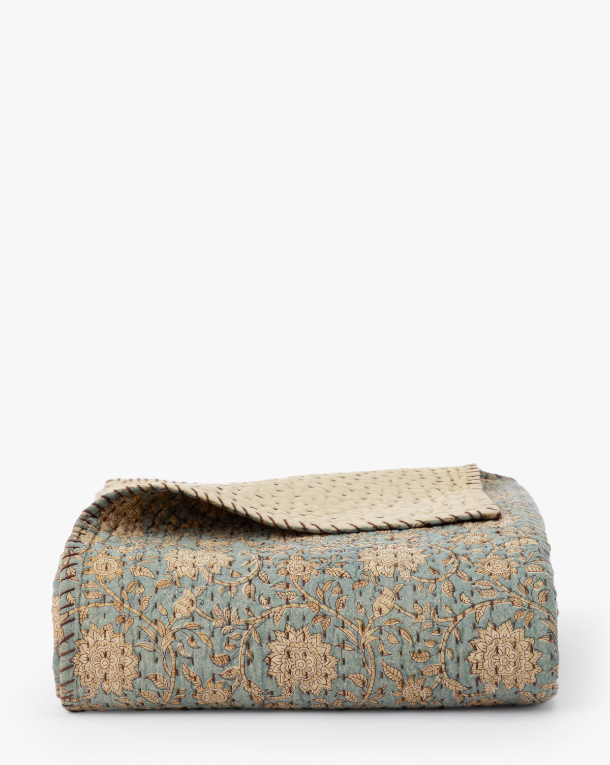 The Gabriella Block Print Quilt features a blue-green base with intricate gold embroidery, a beige underside with a dotted pattern, and is displayed against a plain white background.