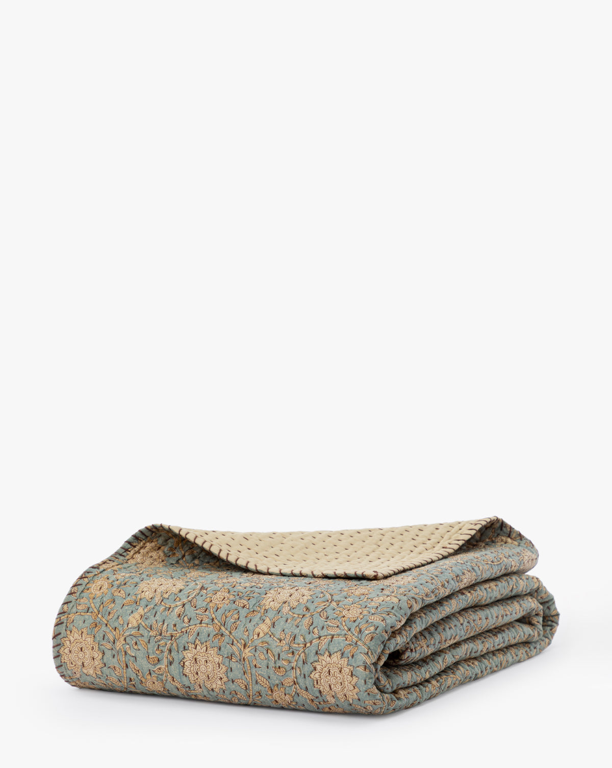 The Gabriella Block Print Quilt, featuring a folded blue and beige floral pattern on cotton with a cream underside, is displayed against a plain white background.