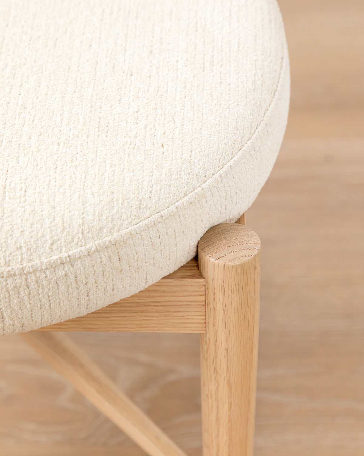 Close-up of the Garance Dining Chair, featuring light beige performance velvet upholstery, rounded edges, and a light wood frame and legs. The wooden floor beneath complements the chair’s natural tones, by McGee & Co.