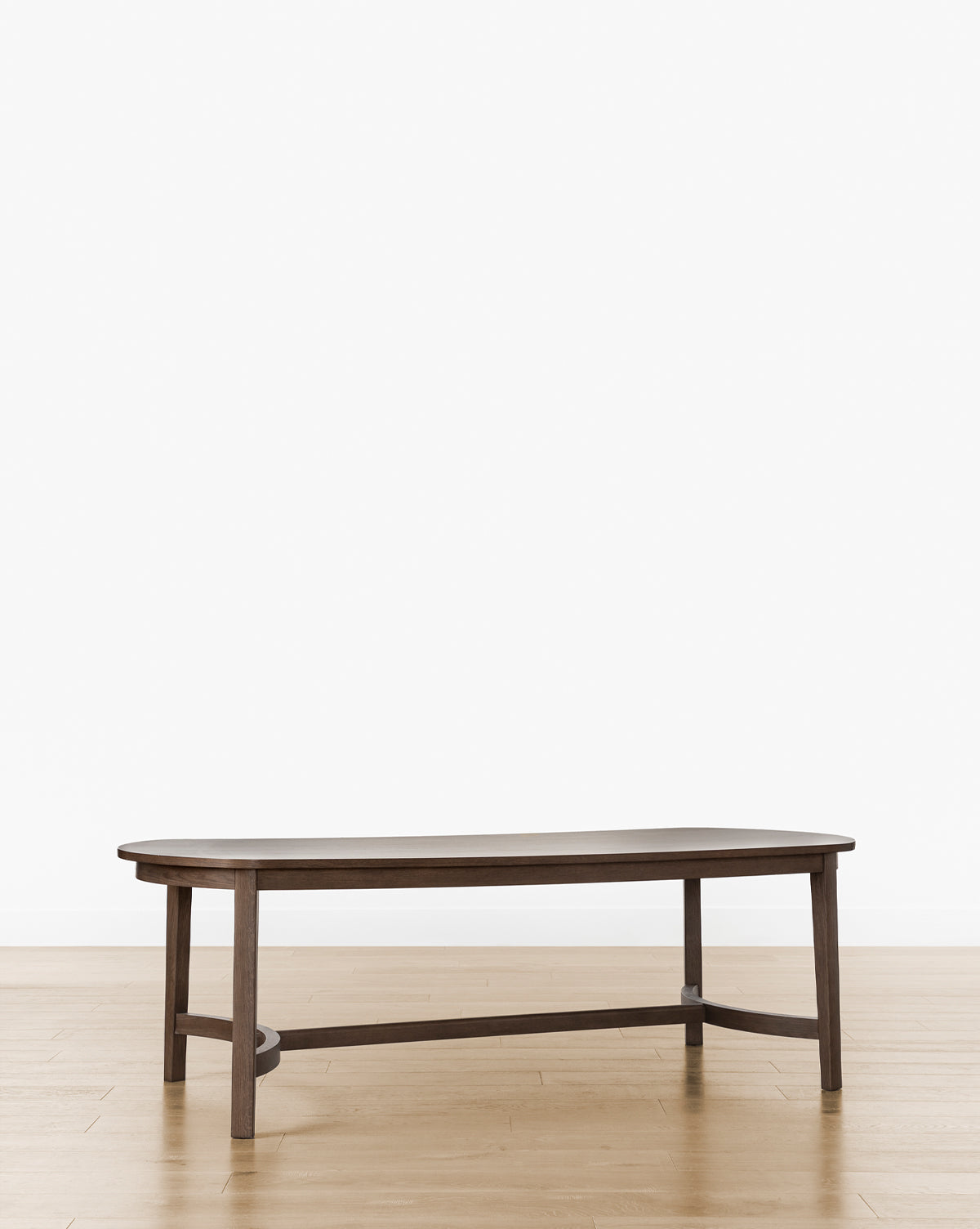 The Gardiner Dining Table features a modern design with a dark Walnut Oak finish, an irregular oval top, and angled legs, by McGee & Co. It is shown on a light wood floor against a plain white background.