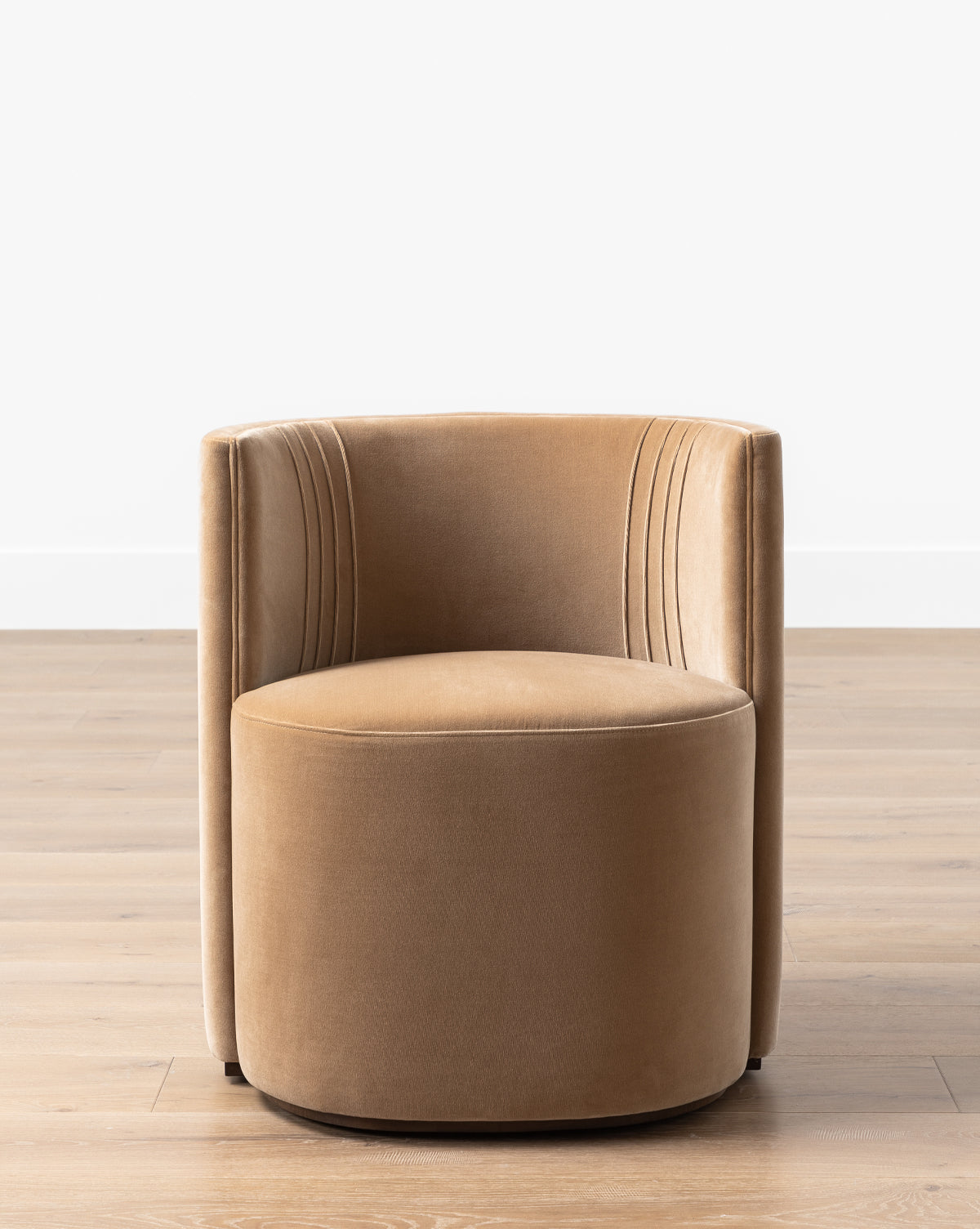 A modern tan Georgina Dining Chair (Ready to Ship) with a curved back and vertical stitching sits on a light wood floor against a white wall, by McGee & Co.