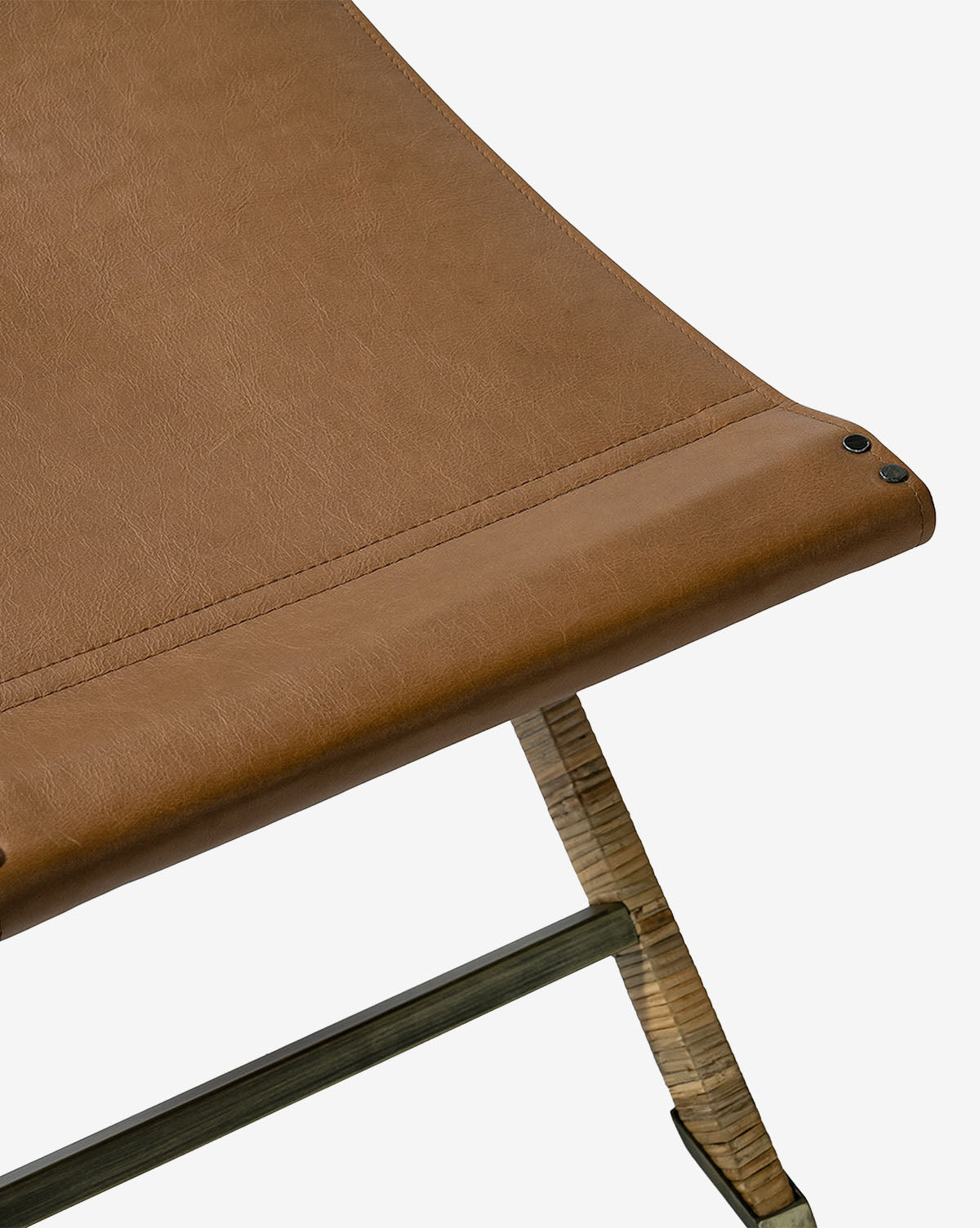 Close-up of the Palecek Gertie Stool featuring a brown leather seat, wooden legs, visible stitching, and three black rivets at the corner, shown against a white background. McGee & Co.