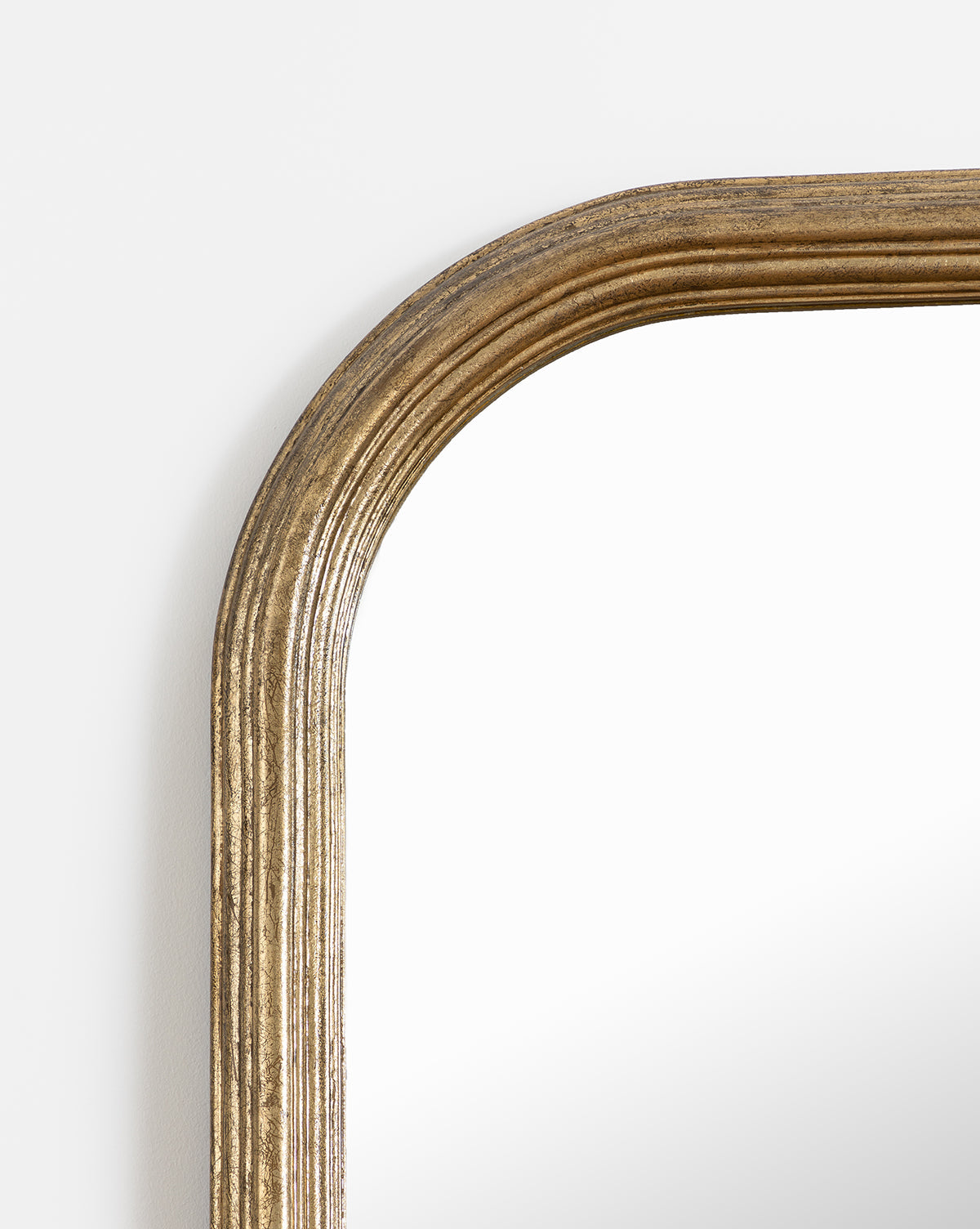 Close-up of the top left corner of the Giada Floor Mirror, featuring a rectangular design with an elegant gold ridged frame and rounded edges, set against a plain white background, by McGee & Co.