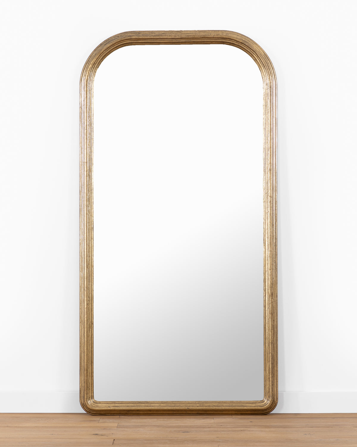 The Giada Floor Mirror showcases a large rectangular design with a rounded top and an elegant gold-toned frame, making it the ideal accent for traditional interiors, by McGee & Co.