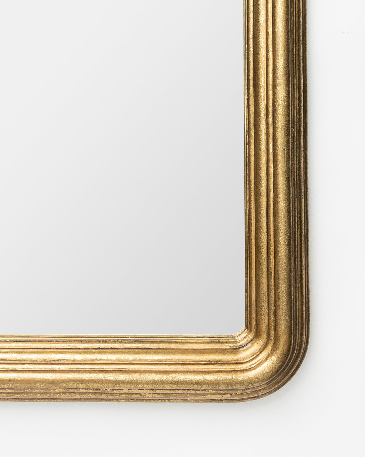 Close-up of the Giada Wall Mirrors bottom right corner, highlighting its wide ridged gold frame. The mirror reflects a soft, neutral background, adding an antiqued touch, by McGee & Co.