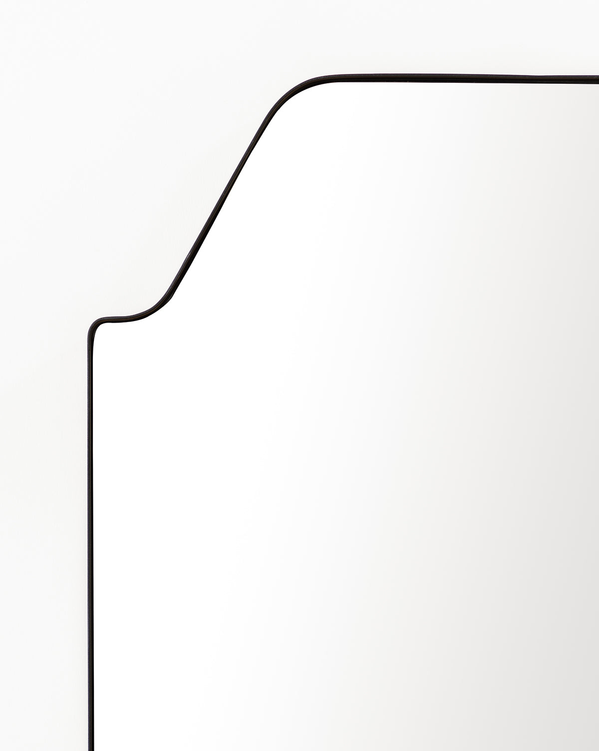 A close-up of the Giles Floor Mirror—a rectangular design with rounded edges and a slim matte black frame—set against a white background. Only part of the upper left section of the mirror is shown by McGee & Co.