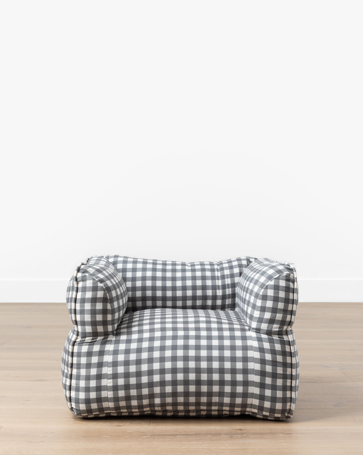 The Gingham Kids Chair features a low, plush design with black and white gingham fabric, sitting on a light wooden floor against a plain white wall—ideal for any childs room, by McGee & Co.