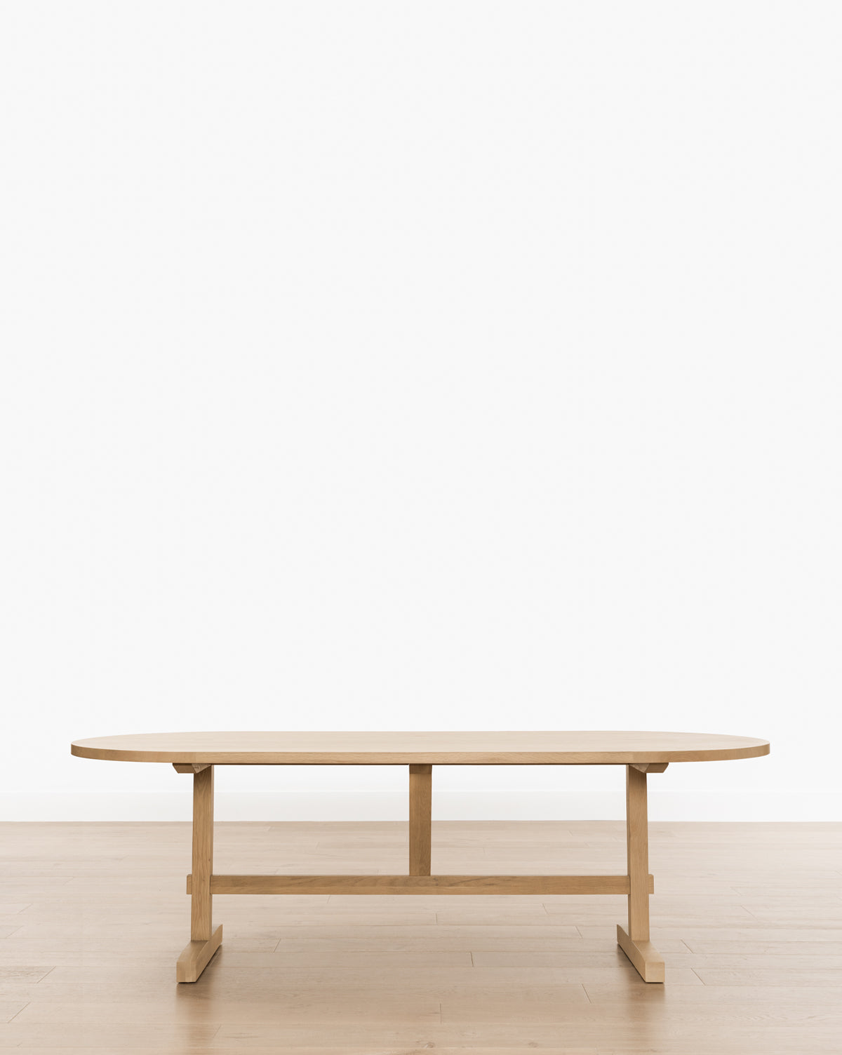The Giselle Oval Dining Table features a minimalist design with rounded edges and a sturdy base, set on a light wood floor against a plain white background, by McGee & Co.