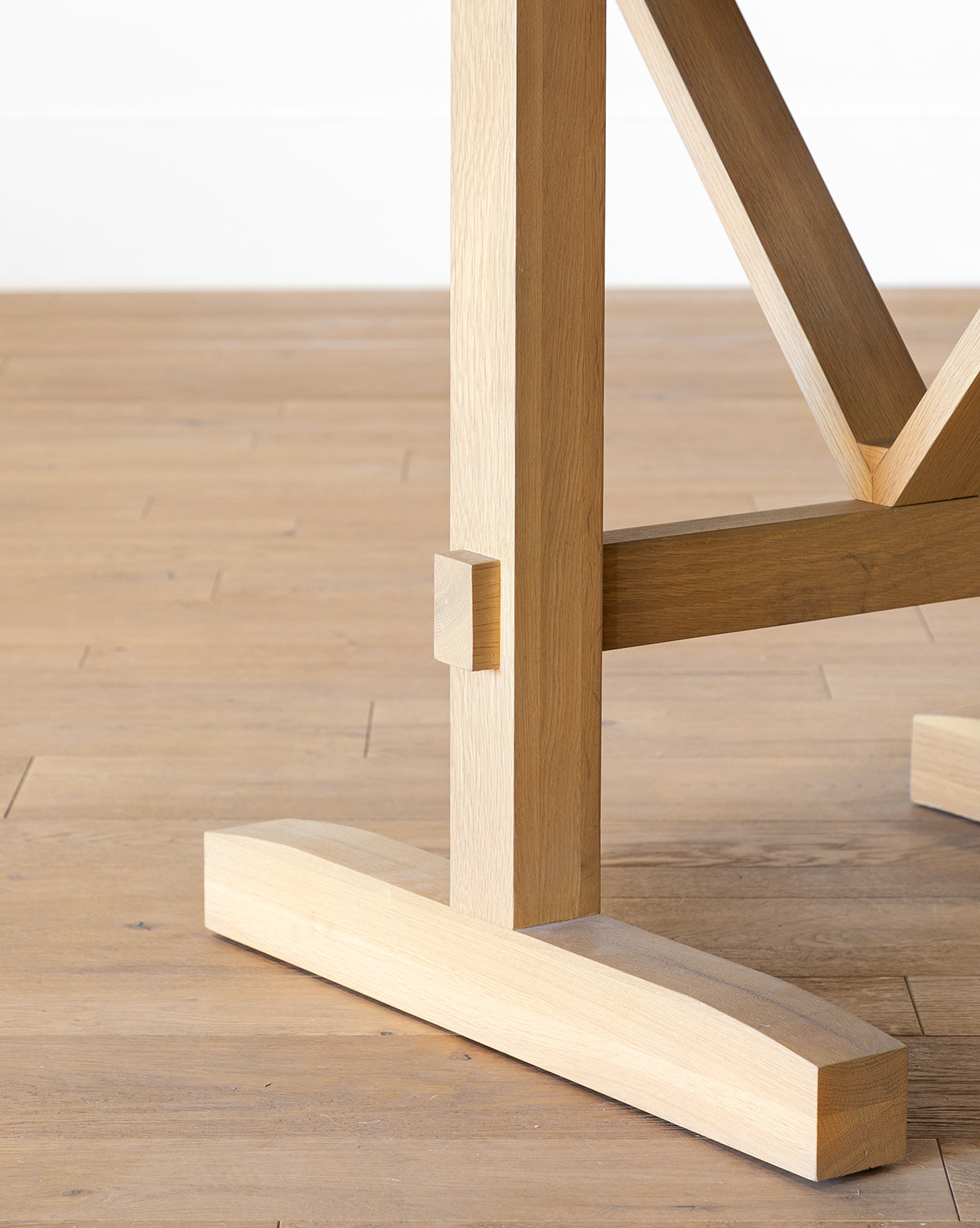 Close-up of the Giselle Round Table’s wooden base on a light wood floor, showcasing its clean lines, sturdy construction, and natural kiln-dried white oak grain, by McGee & Co.