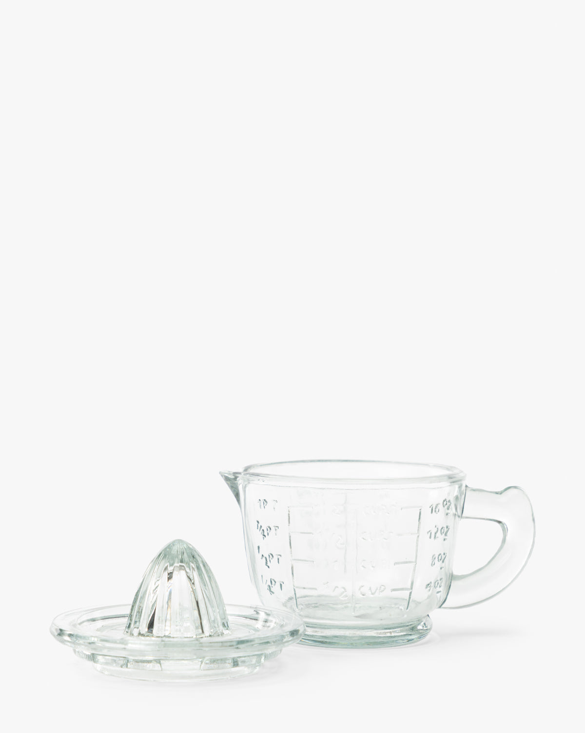 The Glass Juicer with Measuring Cup includes a clear pressed glass citrus juicer with a reamer lid and a matching glass measuring cup featuring a handle and embossed measurements, shown on a white background by McGee & Co.