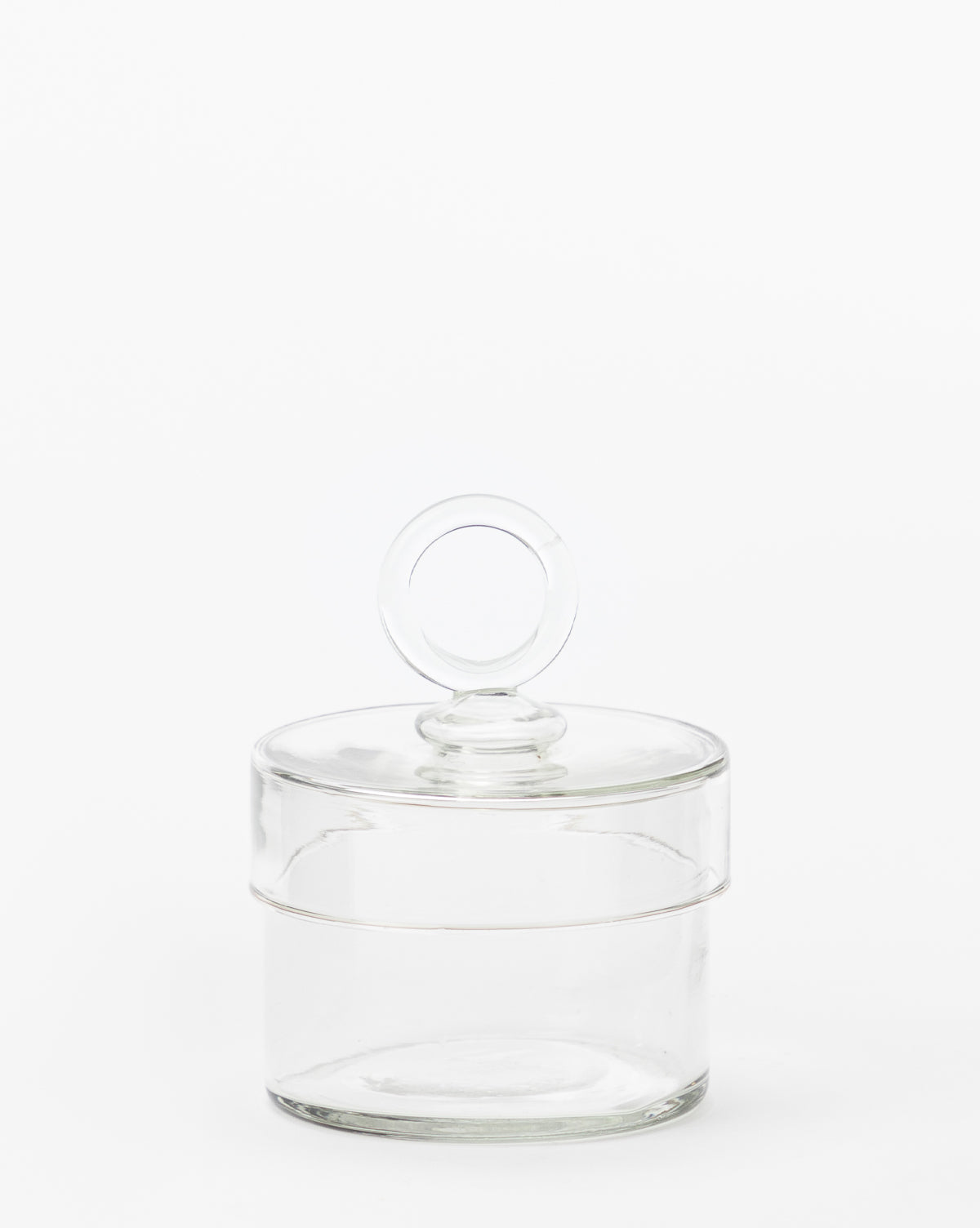 The Glass Lidded Canister, featuring a clear design and matching lid with round handle, is ideal for organizing bathroom essentials on your countertop. Shown against a plain white background.