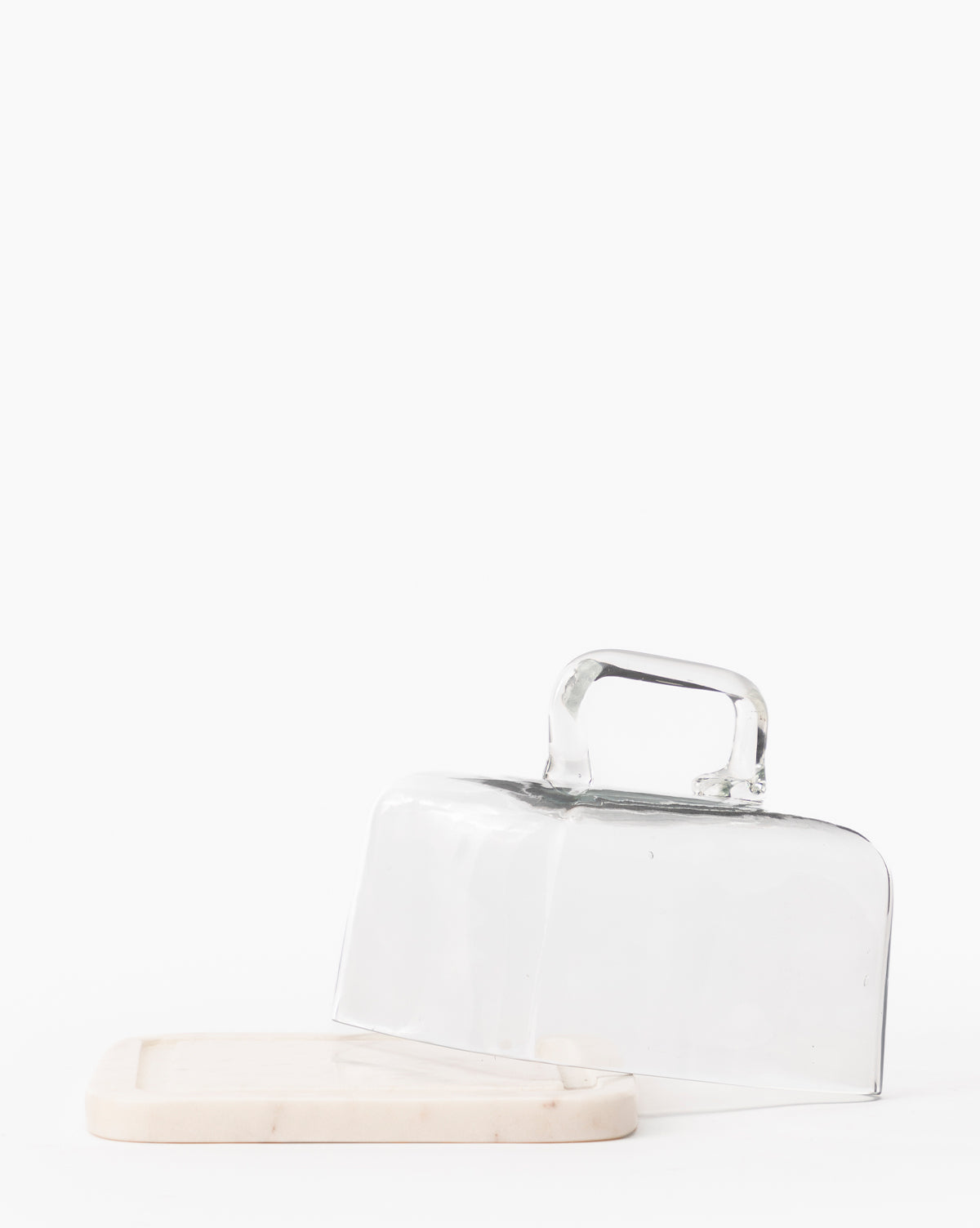 The Glass & Marble Cloche features a clear glass dome with handle tilted on a sleek marble base, creating an elegant kitchen accessory set against a plain white background, by McGee & Co.