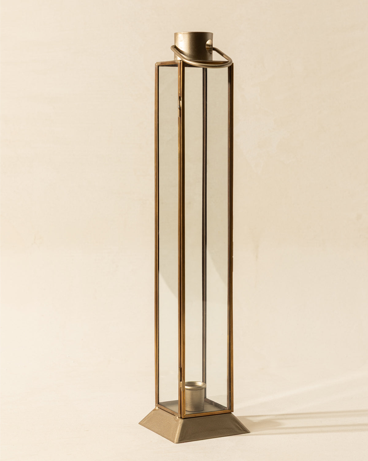 The Glass & Metal Lantern Taper Holder features a tall, rectangular design with a gold frame, wide base, and an inner round taper holder, displayed against a simple light background, by McGee & Co.
