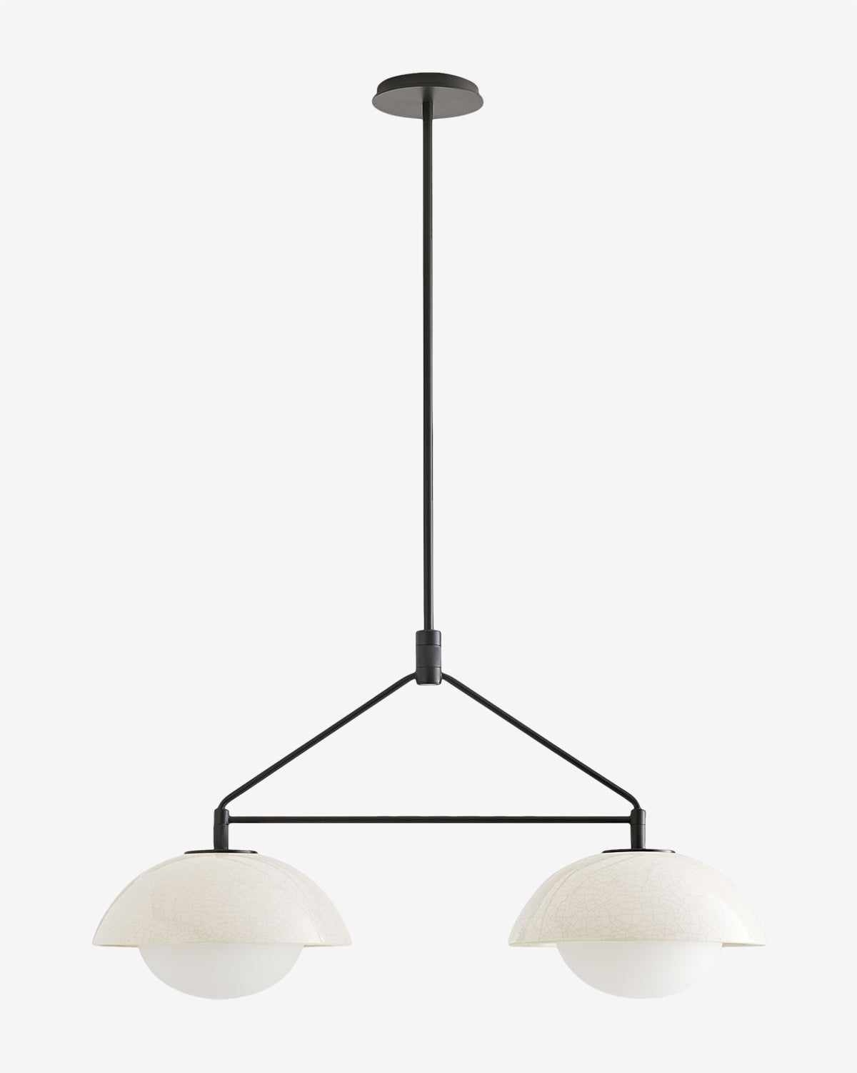 The Arteriors Glaze Linear Pendant features two white globe lamps, each partially covered by a crackled glaze ceramic dome, suspended from a black rod and frame for a modern look. McGee & Co.