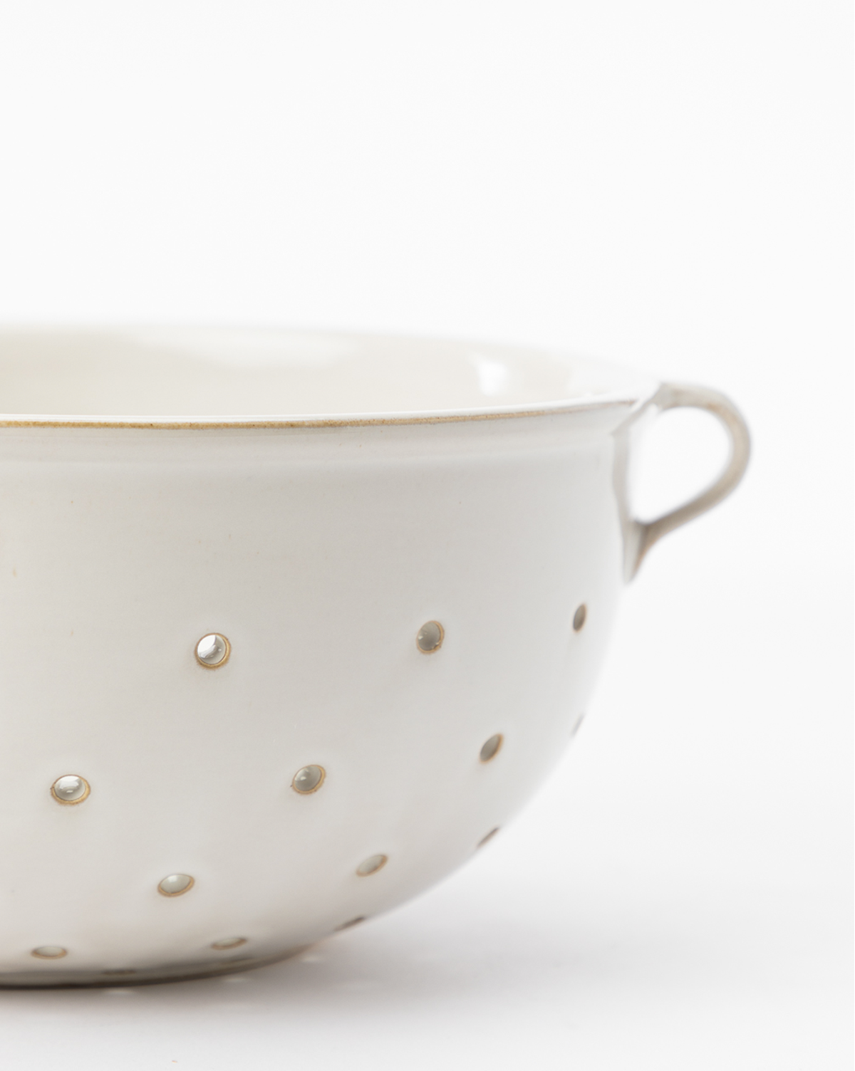 A close-up of a white ceramic Glazed Colander featuring small holes and a handle, ideal for serveware or kitchen decor, shown against a plain white background, by McGee & Co.