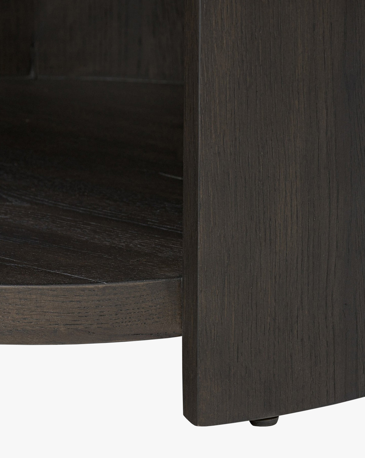 Close-up of the lower corner of the Glenndon Oak Nightstand, featuring a black oak finish with visible wood grain, curved base, vertical panel, and a small black floor protector by McGee & Co.