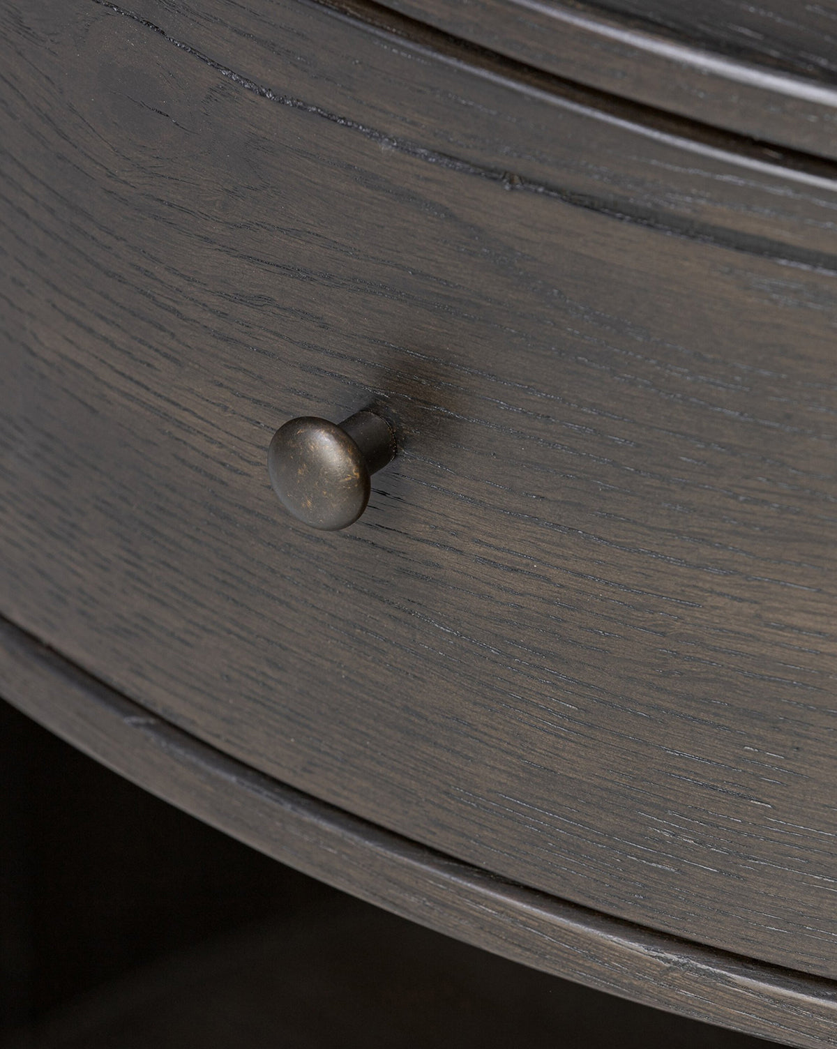 Close-up of the Glenndon Oak Nightstand’s black-finished drawer, featuring a round metal knob. The elegant wood grain and slightly curved front bring modern sophistication to this bedside table by McGee & Co.