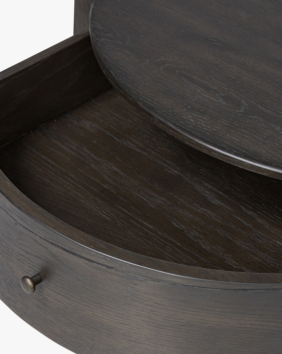 Close-up of the Glenndon Oak Nightstand’s black-finished drawer with an open rounded front, showcasing the wood grain texture and a metallic knob handle on the left side, by McGee & Co.