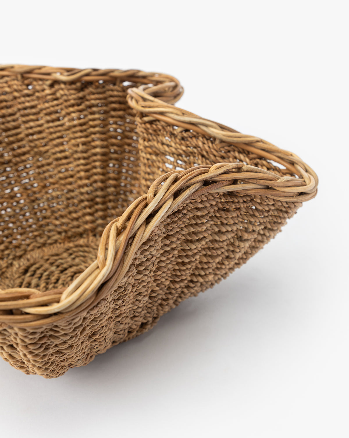 A close-up of the Goulding Woven Bowl—a square rattan basket with curved, braided edges—ideal as entryway decor or a stylish wicker bowl, shown against a plain white background, by McGee & Co.