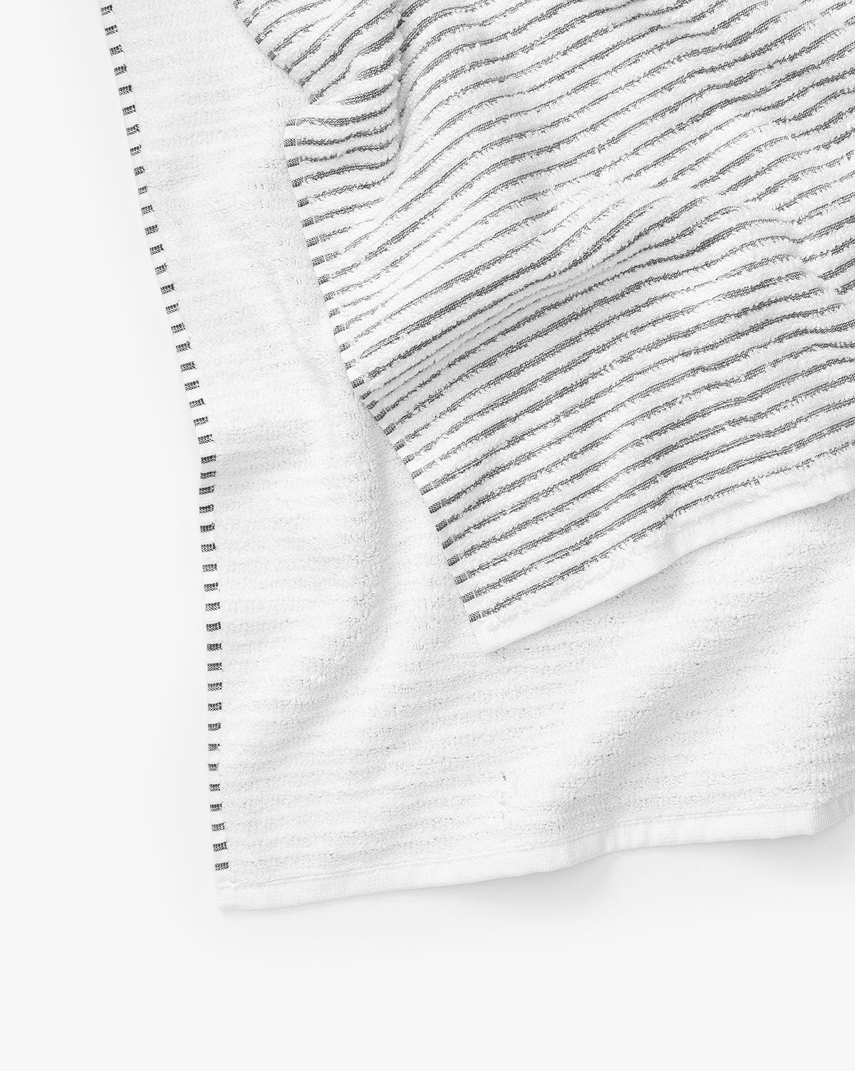 A close-up of two absorbent Gray Striped Bath Collection towels made from Aegean cotton. One towel lies flat while the other is crumpled on top, both featuring thin dark stripes and a soft, textured look against a white background.
