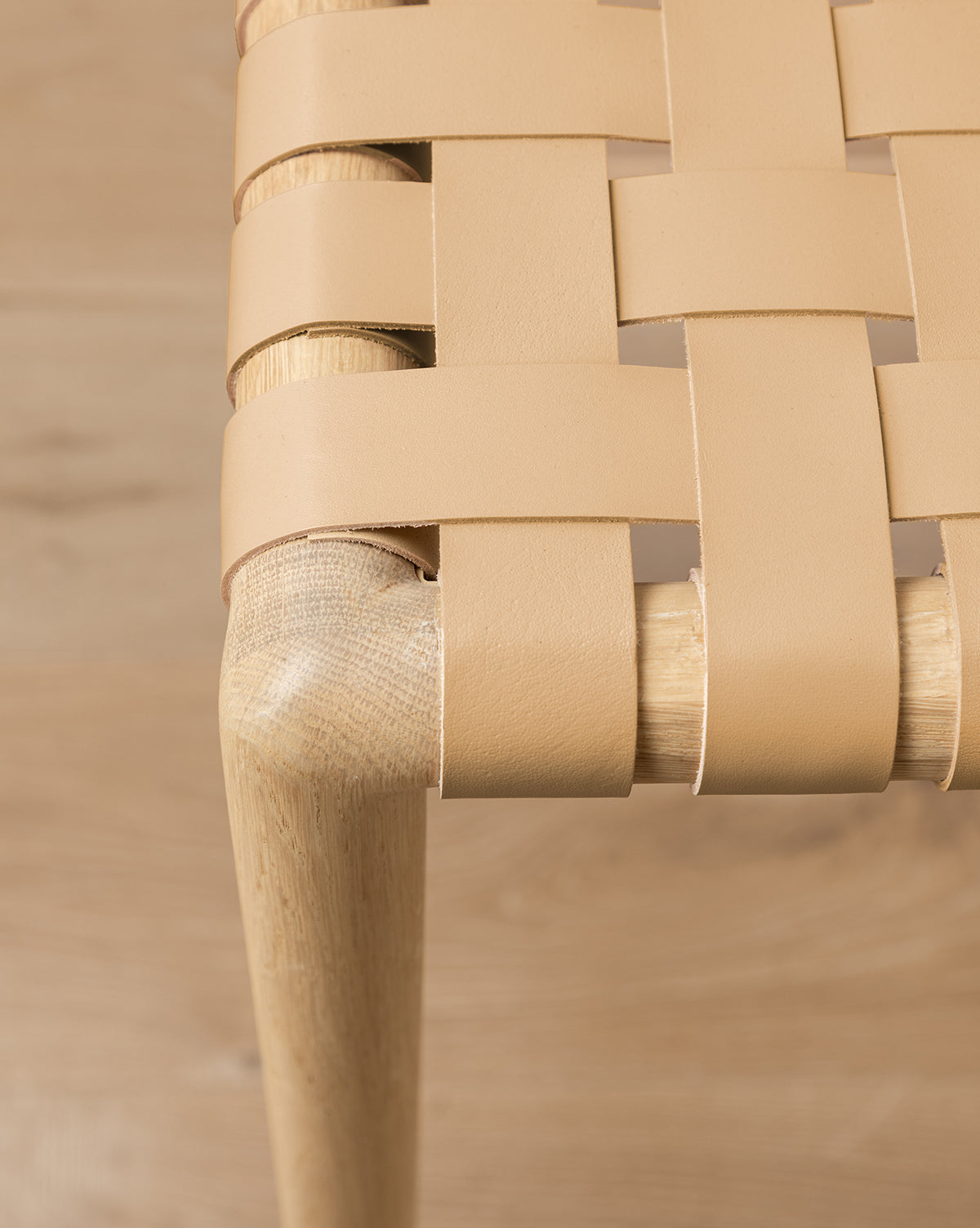 Close-up view of the Greely Stool, featuring a woven light tan aniline-dyed leather seat and a wooden leg, highlighting the interlacing pattern and smooth wood grain by McGee & Co.