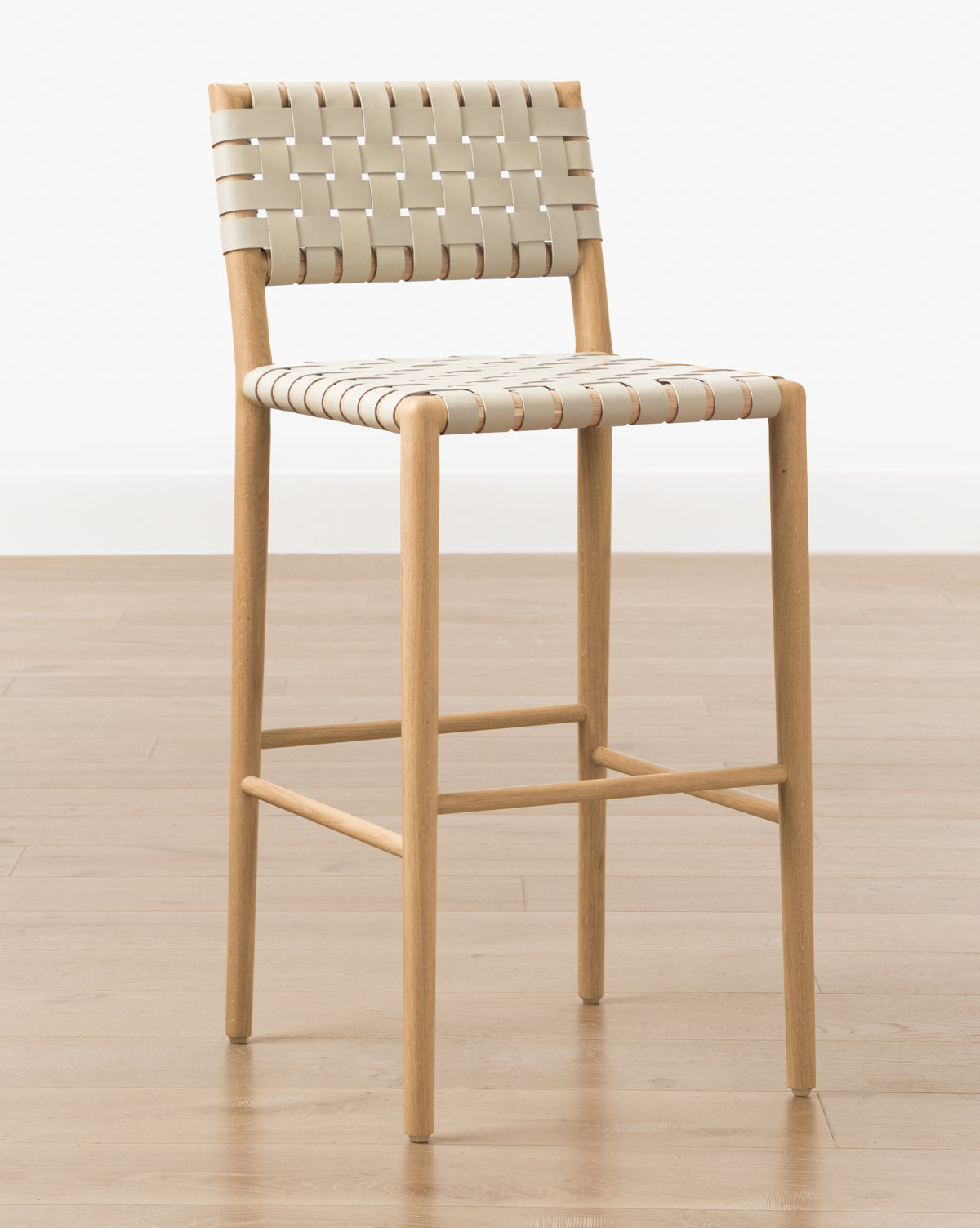 The Greely Stool features a modern design with a white oak frame and cream woven seat and back, shown on a light wood floor against a white wall, by McGee & Co.