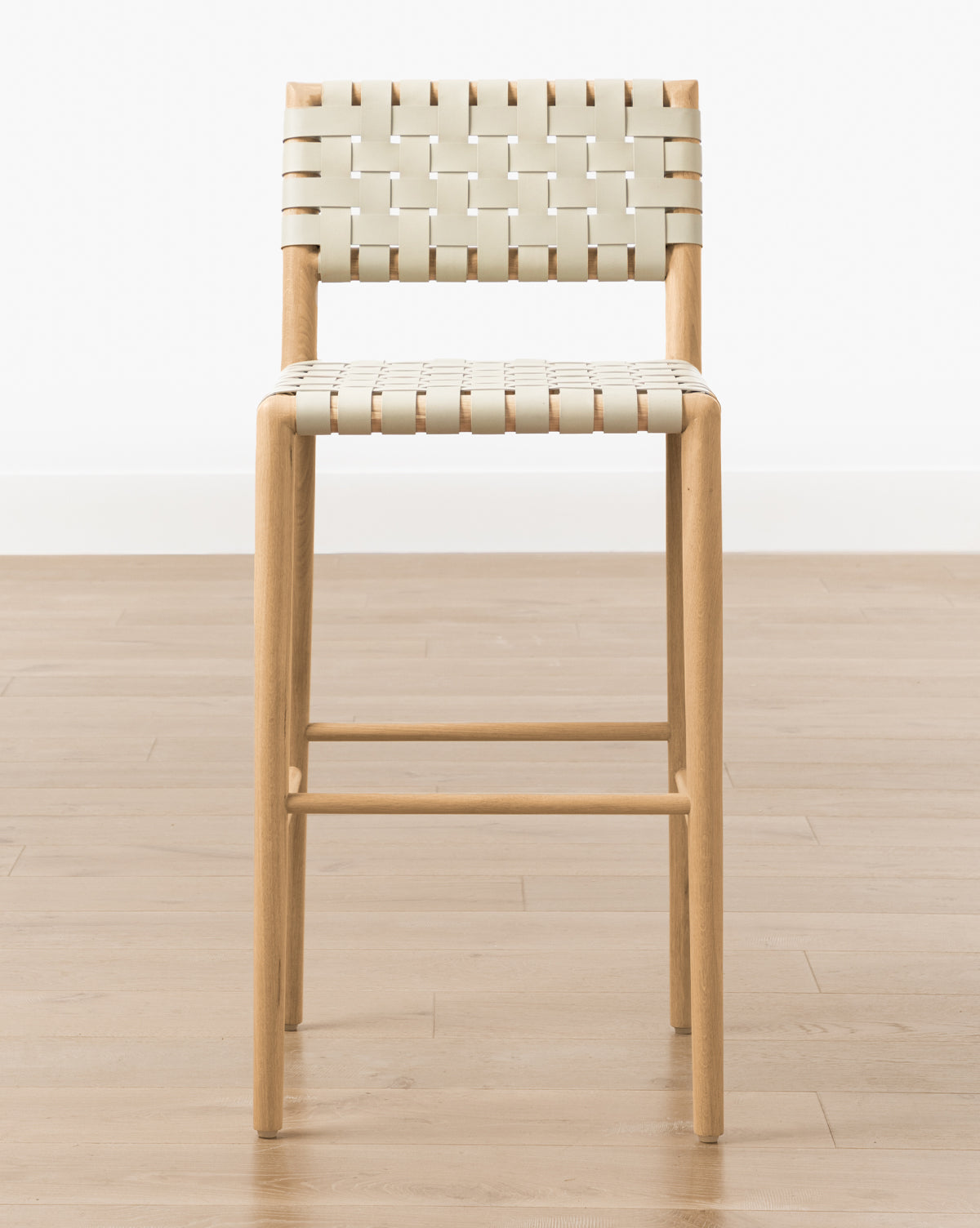 The Greely Stool, with its cream woven seat and backrest, features a sturdy white oak frame and sits on a light wood floor against a white wall, by McGee & Co.