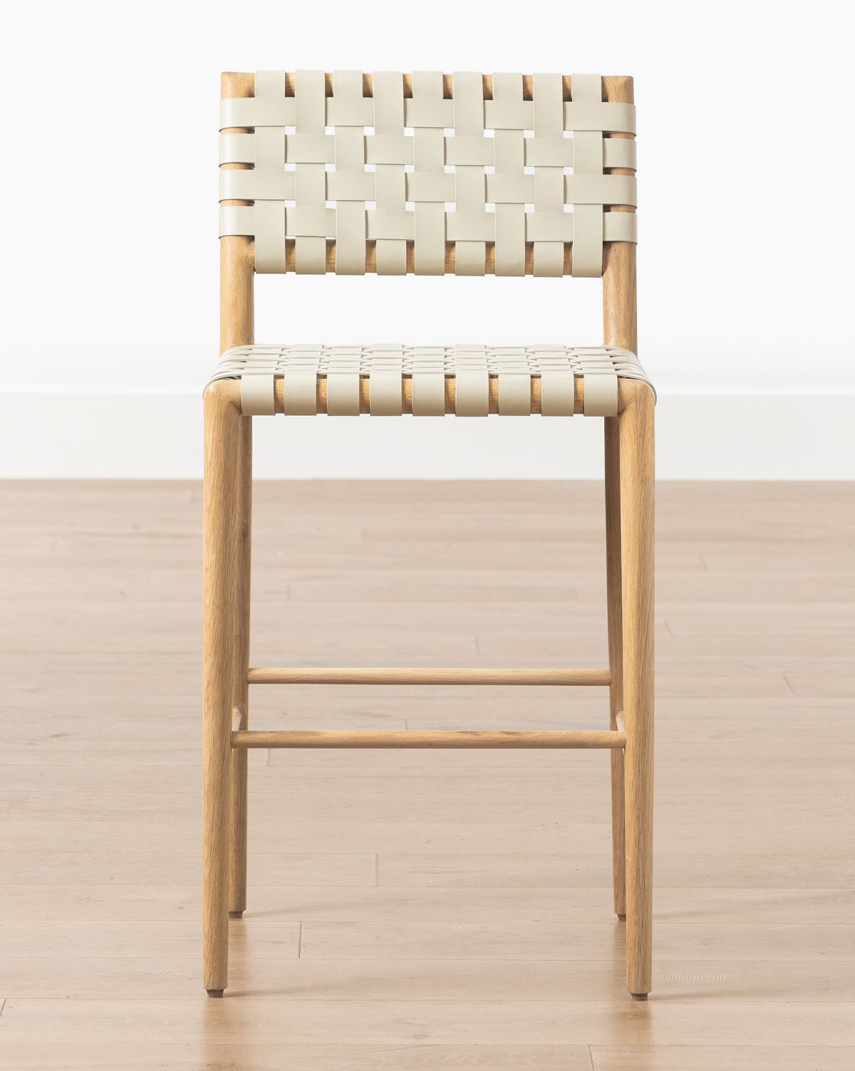 The Greely Stool features a cream woven seat and backrest, a sturdy white oak frame with four straight legs, and a footrest, shown on a light wood floor against a plain white background by McGee & Co.