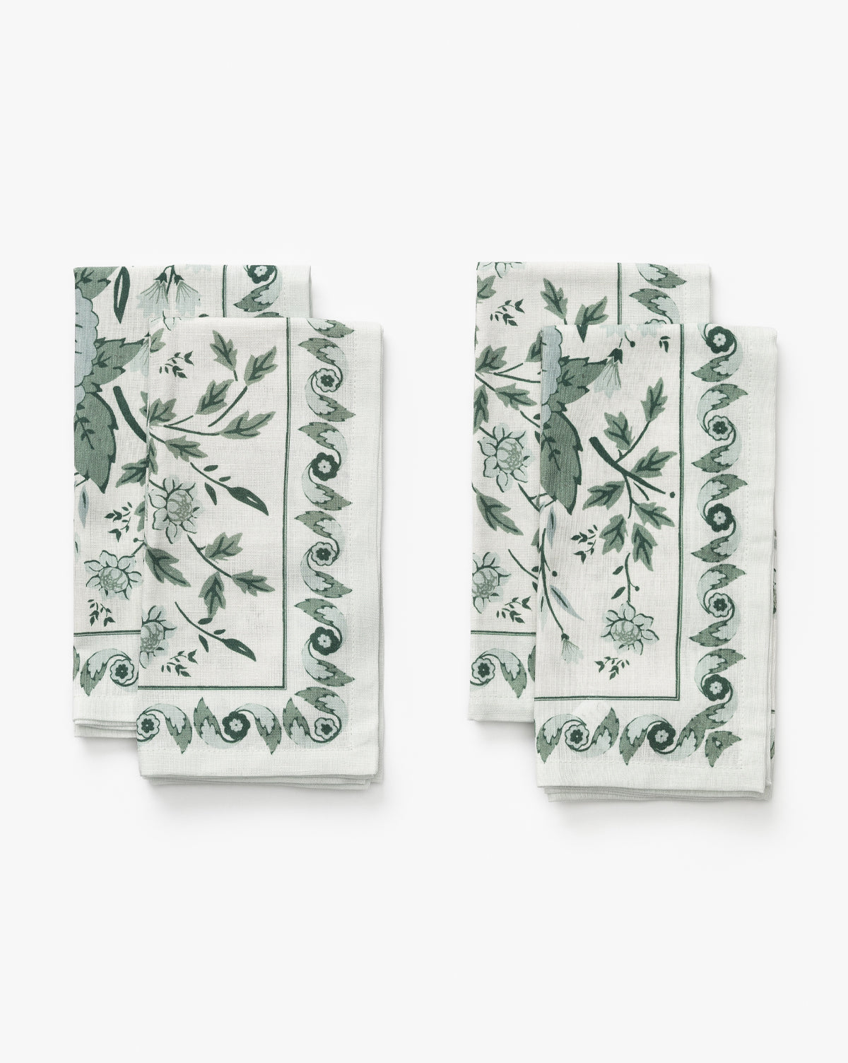 Two neatly folded cotton-flax napkins from the Halcyon Napkin Set (Set of 4), featuring a green floral and leaf print with a swirl border, are displayed side by side on a light background, by McGee & Co.