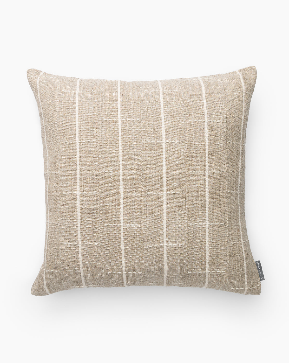 The Hamilton Pillow Cover is a square beige cotton matelasse pillow cover with subtle textured fabric, featuring thin vertical white stitched lines and a small side fabric tag, shown against a white background by McGee & Co.