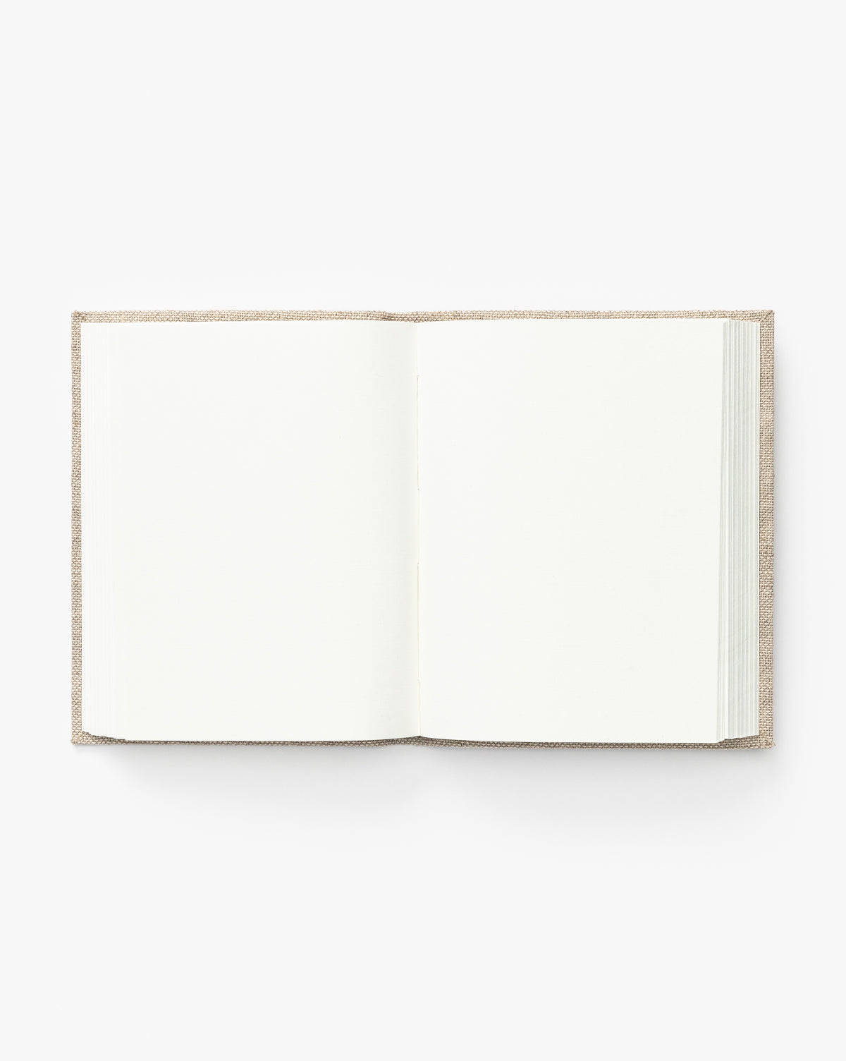 A Handcrafted Linen Book with a textured light brown hardcover opens flat to reveal two blank white pages against a plain background, showcasing the timeless elegance of traditional linen binding.