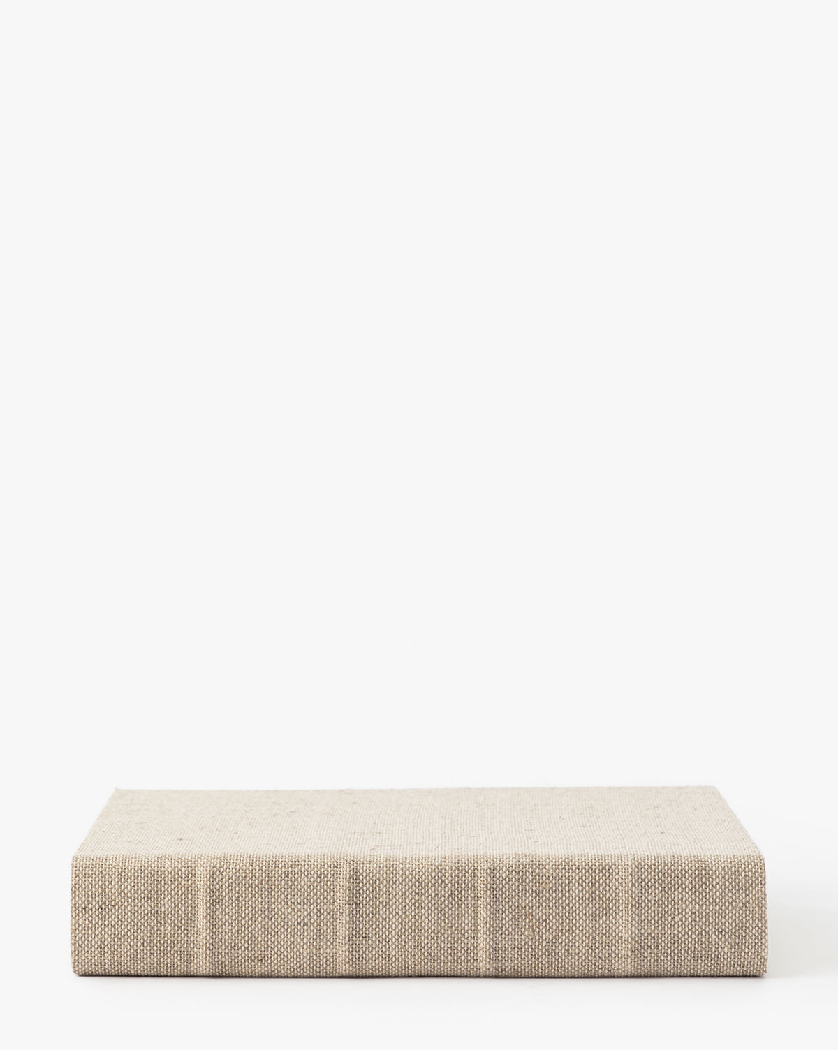 The Handcrafted Linen Book is a thick, closed hardcover with a textured beige linen fabric cover, shown lying flat on a plain white background.