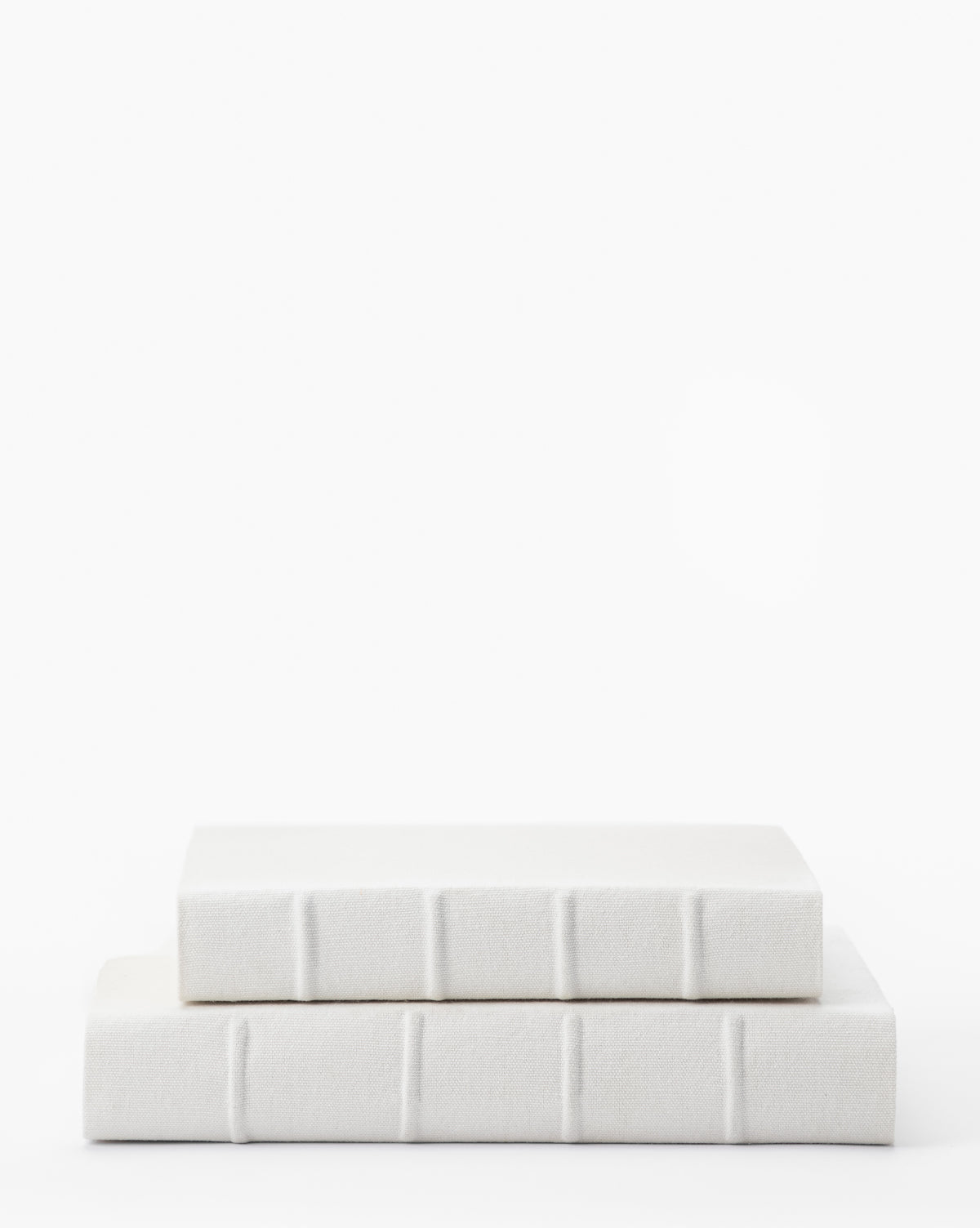 Two Handcrafted Linen Books with white covers and textured spines are stacked against a plain white background, highlighting their traditional binding and the elegant charm of linen fabric.