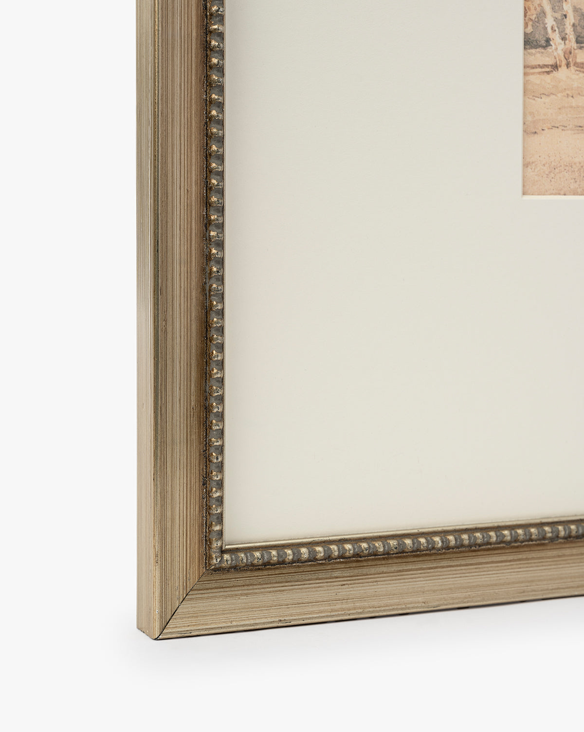 Close-up of the Harewood Park frame corner in distressed silver with a metallic finish and beaded detailing, shown holding matted artwork or a giclee print against a white background, by McGee & Co.