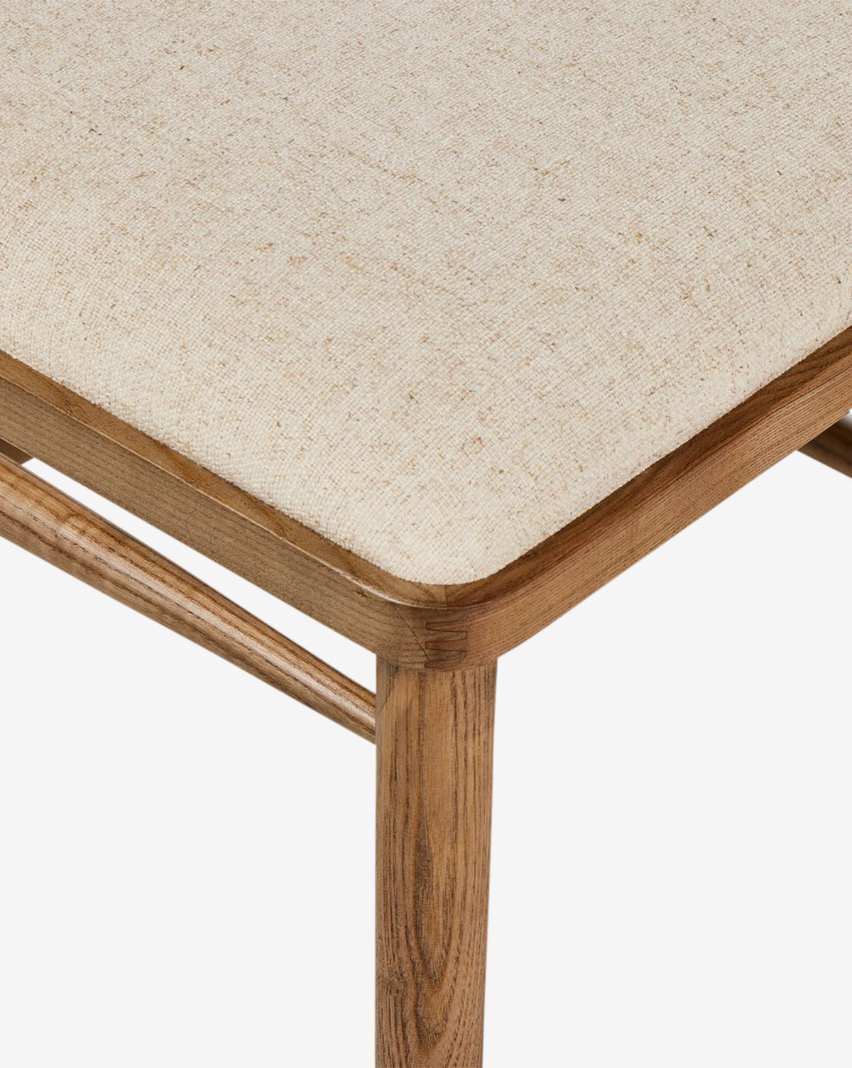 Close-up of the Harper Dining Chair’s corner, showing solid ash wood construction with a light beige upholstered seat cushion and smooth, rounded edges, by McGee & Co.