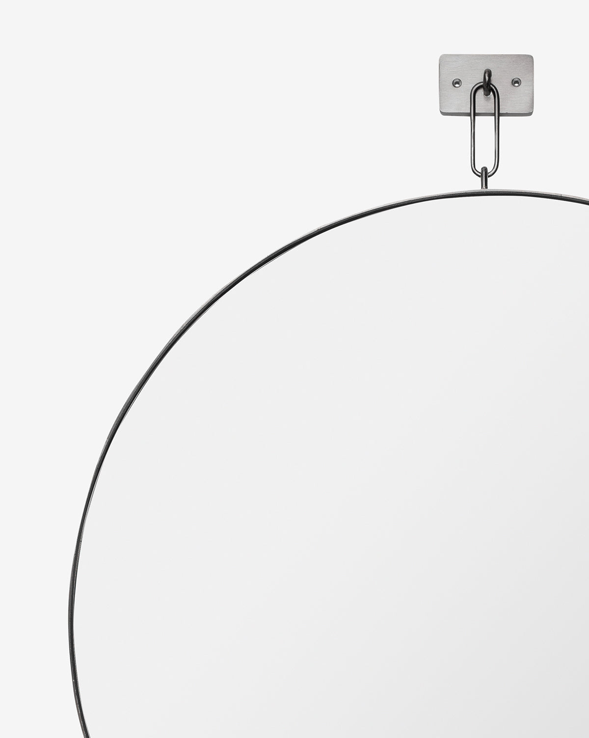 The Haven Wall Mirror features a modern thin black frame and hangs from a rectangular stainless steel wall mount and chain against a plain white background, with only the upper portion of the mirror visible, by McGee & Co.
