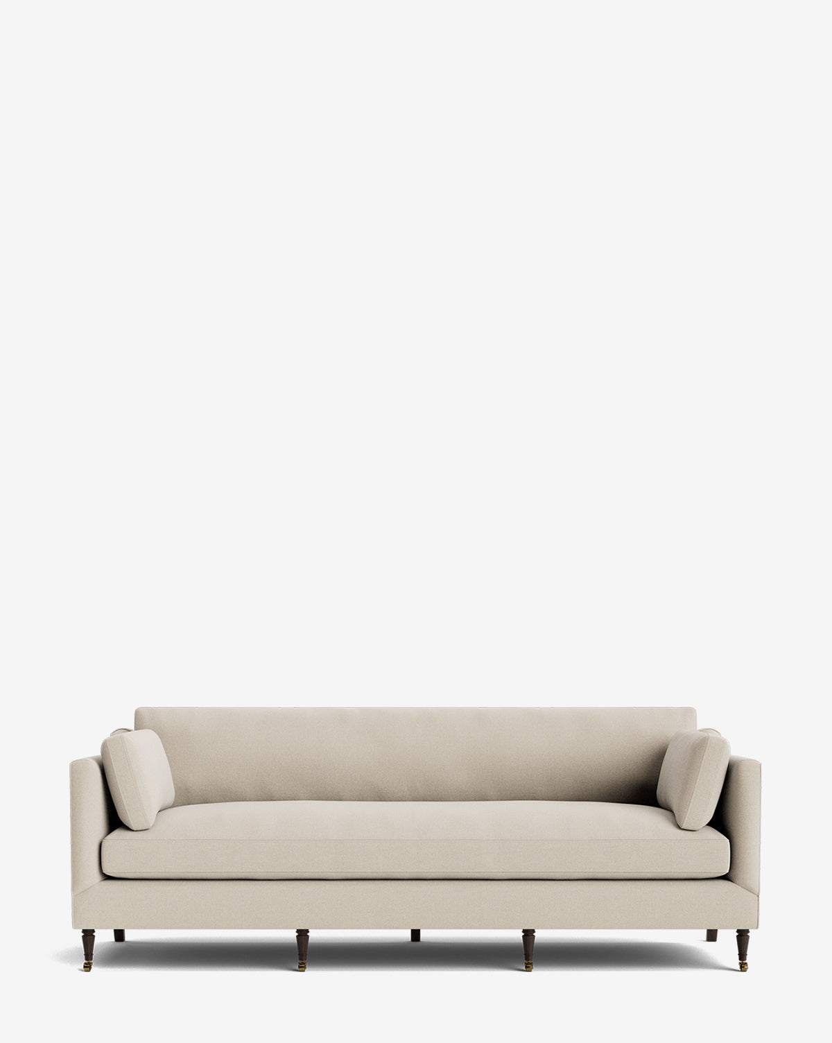 The Haverford Upholstered Sofa 90 is a beige, modern handcrafted sofa with a straight back, two matching cylindrical cushions, and slim wooden legs with brass castors, pictured against a plain white background by McGee & Co.