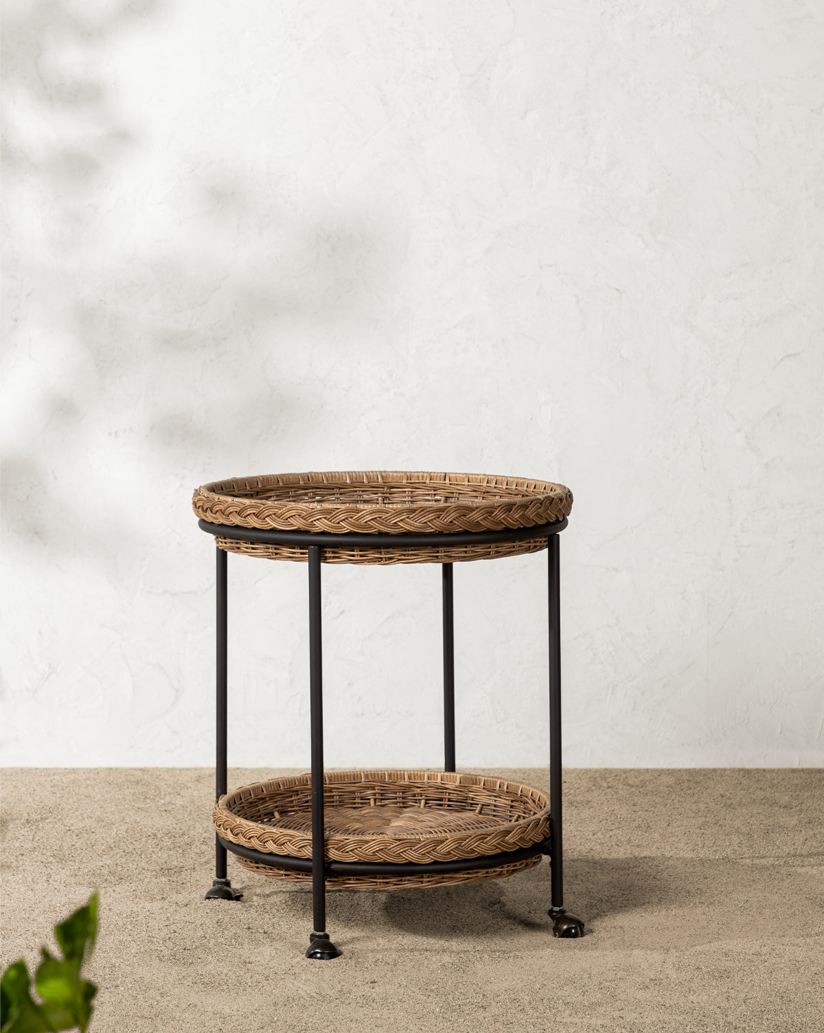 Close-up of the Haviland Bar Cart featuring weather-resistant round wicker with a braided edge, black metal legs, and a tightly woven surface—ideal for outdoor entertaining against a blurred gravel or pebble ground, by McGee & Co.