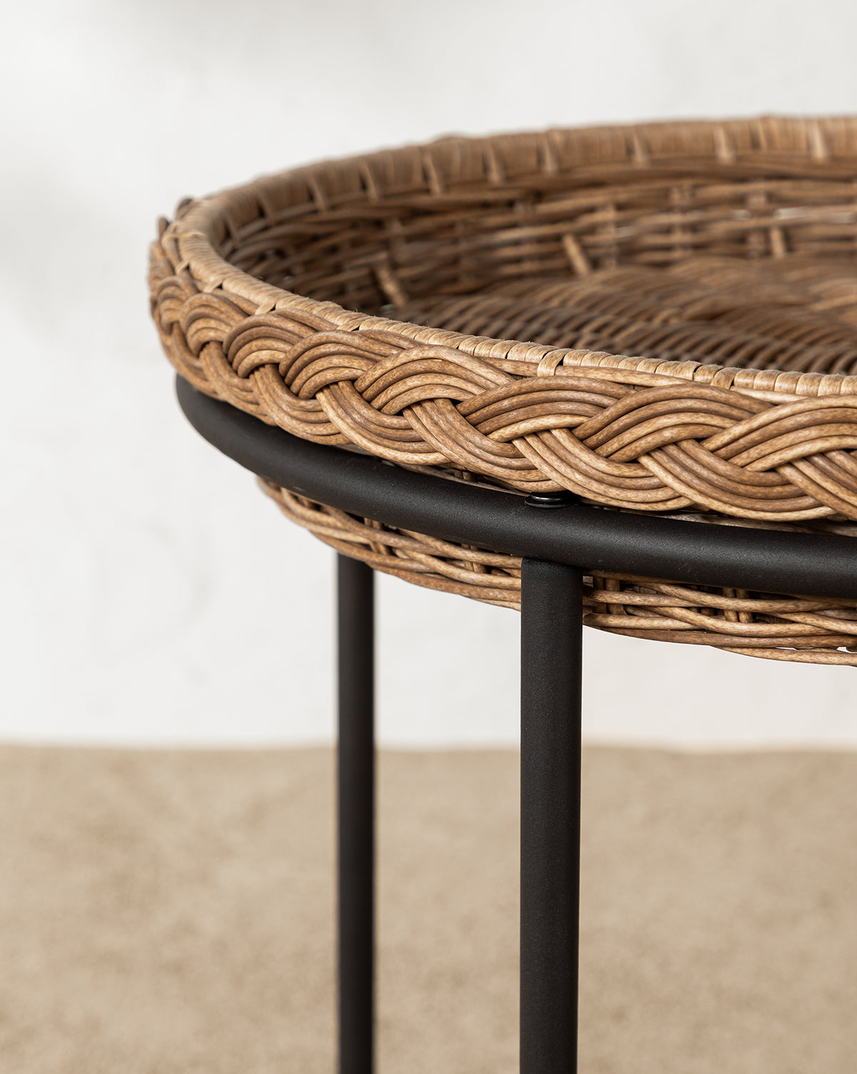 A close-up of the Haviland Bar Cart featuring weather-resistant wicker, a black metal frame, and caster wheels, set on a bed of small, light-colored pebbles, by McGee & Co.