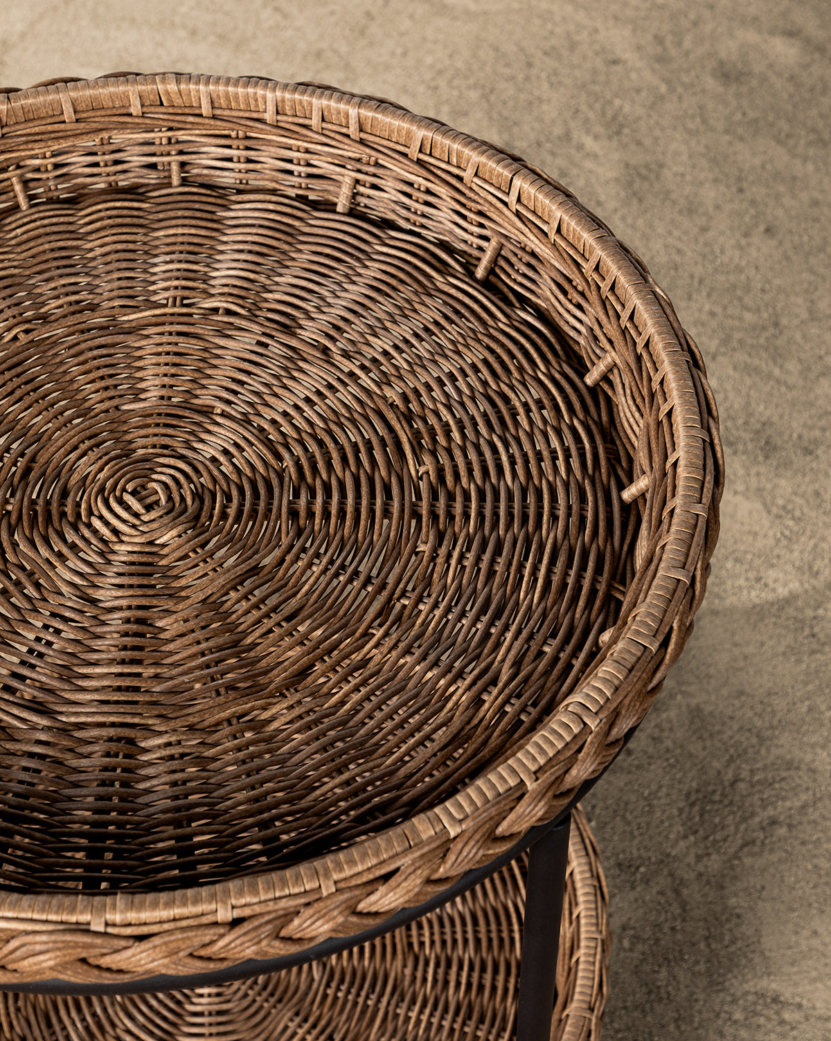 The Haviland Bar Cart features weather-resistant wicker with two round tiers and sturdy black metal legs, set on small white stones against a light textured wall—ideal for outdoor entertaining, by McGee & Co.