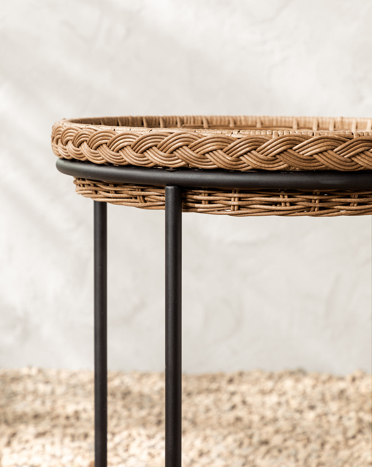 A close-up of the Haviland Bar Cart, featuring weather-resistant wicker with a braided rim and black metal legs, sits on a textured beige surface against a neutral backdrop—perfect for stylish outdoor entertaining, by McGee & Co.