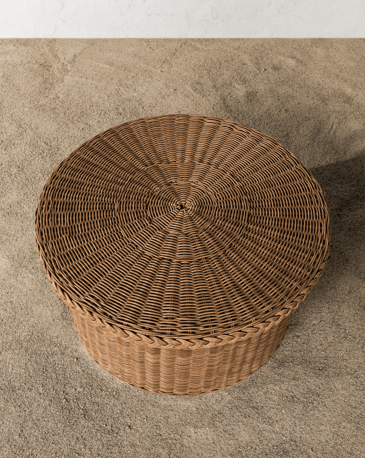 Close-up of the Haviland Coffee Table, a round wicker piece with a braided rim and intricate weaving. This weather-resistant table sits outdoors on small pebbles, by McGee & Co.