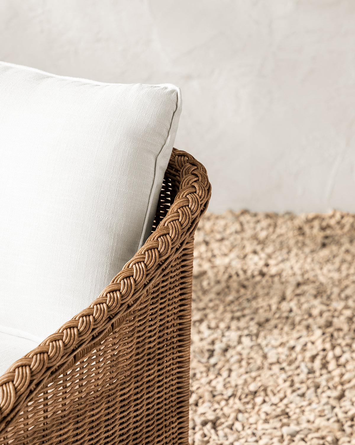 The Haviland Outdoor Dining Chair, crafted from weather-resistant wicker with a white cushion, sits atop a textured beige rug. Its intricate woven design stands out against a light, textured background wall, by McGee & Co.