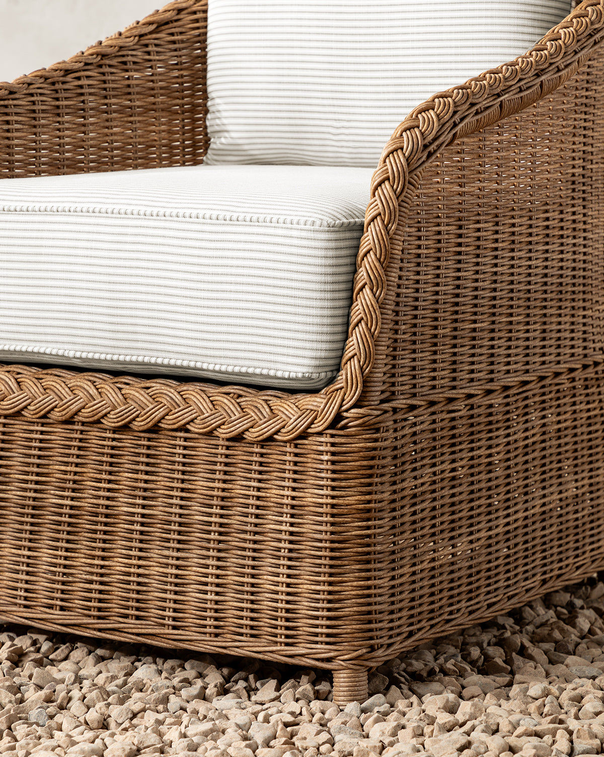A close-up of the Haviland Outdoor Dining Chair with Perennials Taupe Stripe cushions, designed to be weather-resistant, shown on a surface covered in small light-colored pebbles, by McGee & Co.