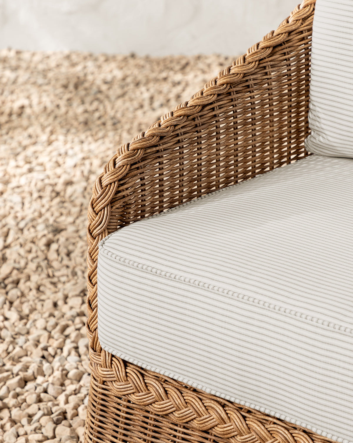 Close-up of the Haviland Outdoor Dining Chair with Perennials Taupe Stripe cushion, featuring weather-resistant wicker, braided edge detail, and woven texture, set on light-colored pebbles by McGee & Co.