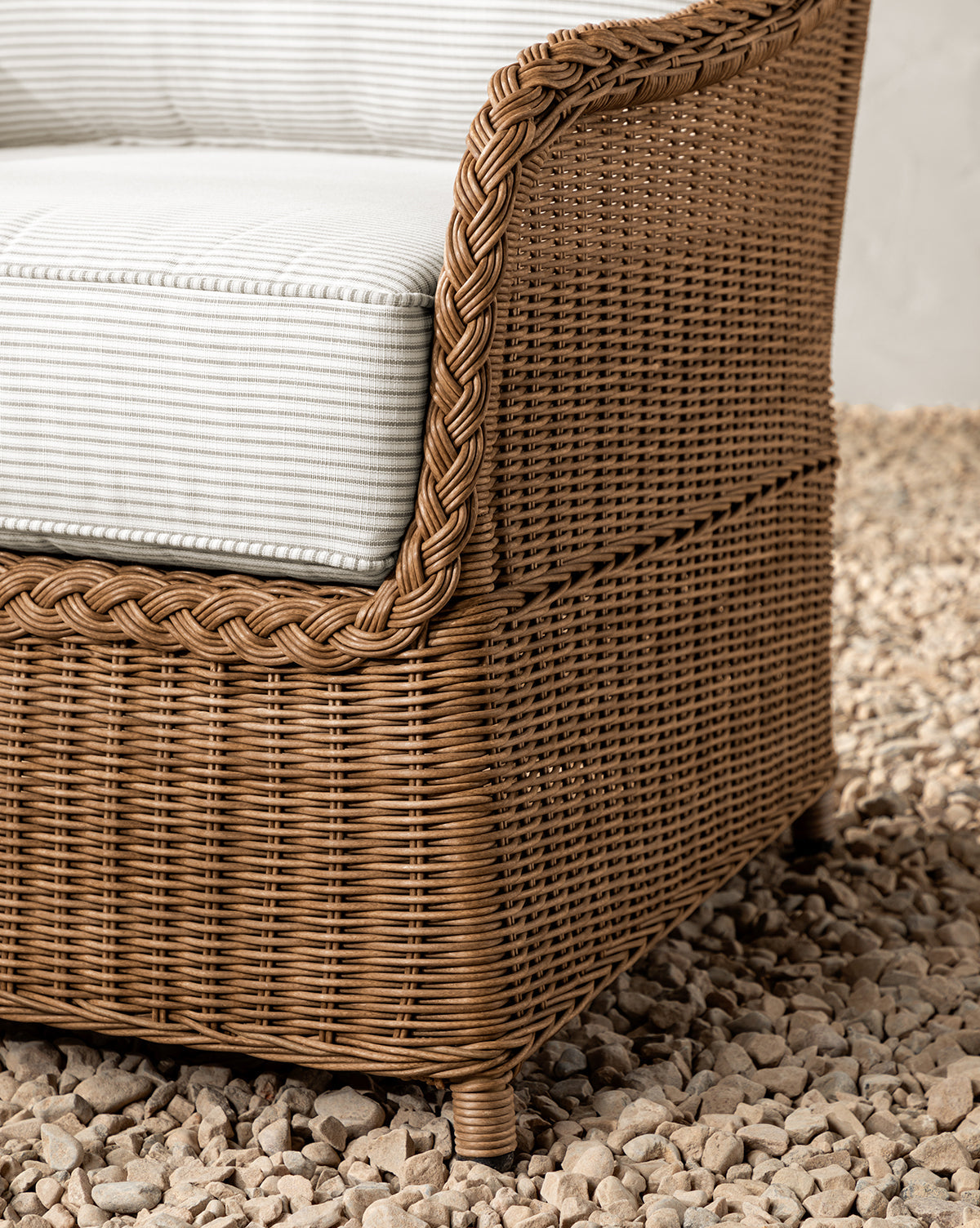 Close-up of the Haviland Outdoor Lounge Chair with a weather-resistant wicker frame and a thick Perennials Taupe Stripe cushion, set on light-colored pebbles, by McGee & Co.