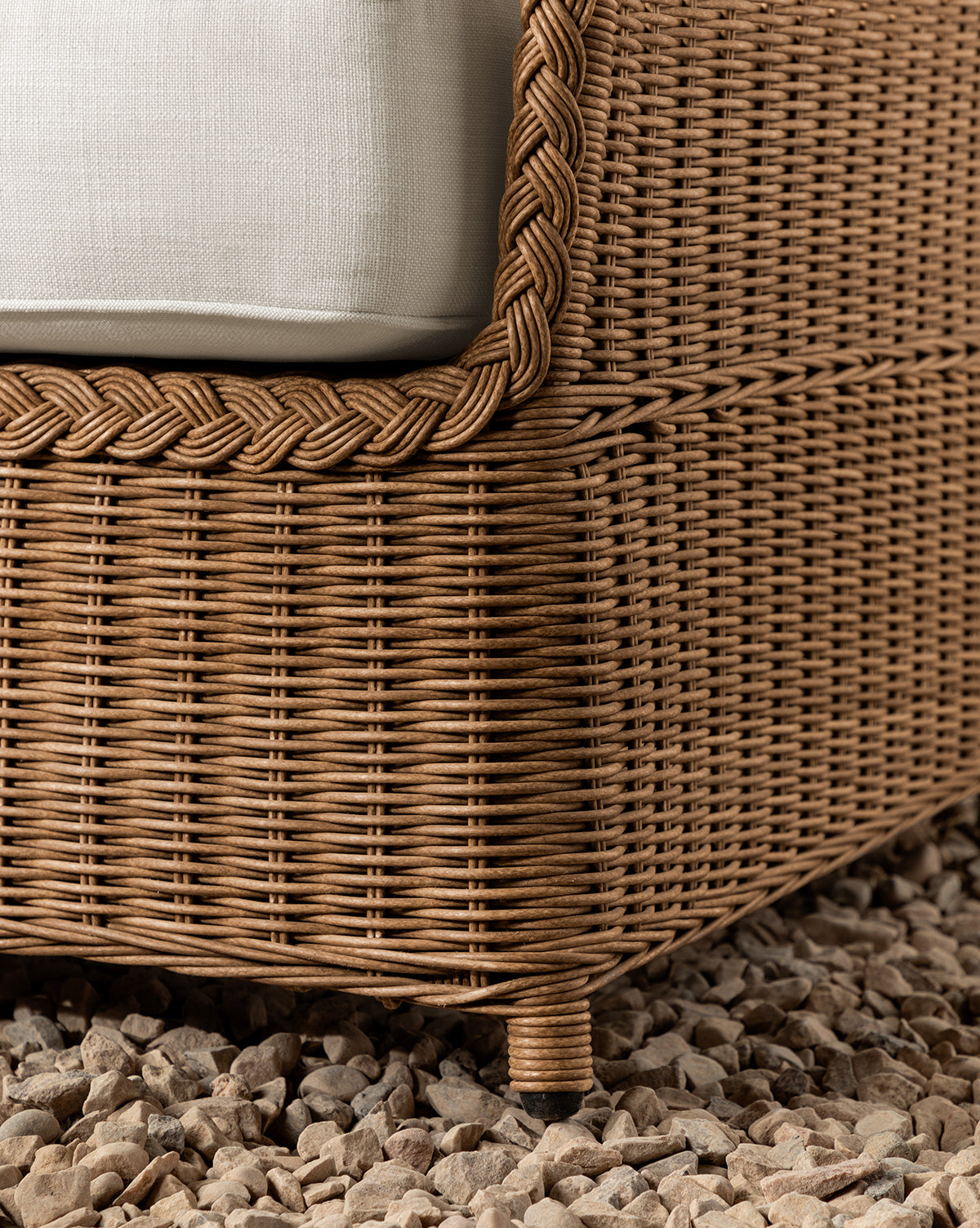 Close-up of a corner of the Haviland Outdoor Sofa 88, featuring weather-resistant wicker with braided trim and a white cushion, set on light-colored pebbles by McGee & Co.
