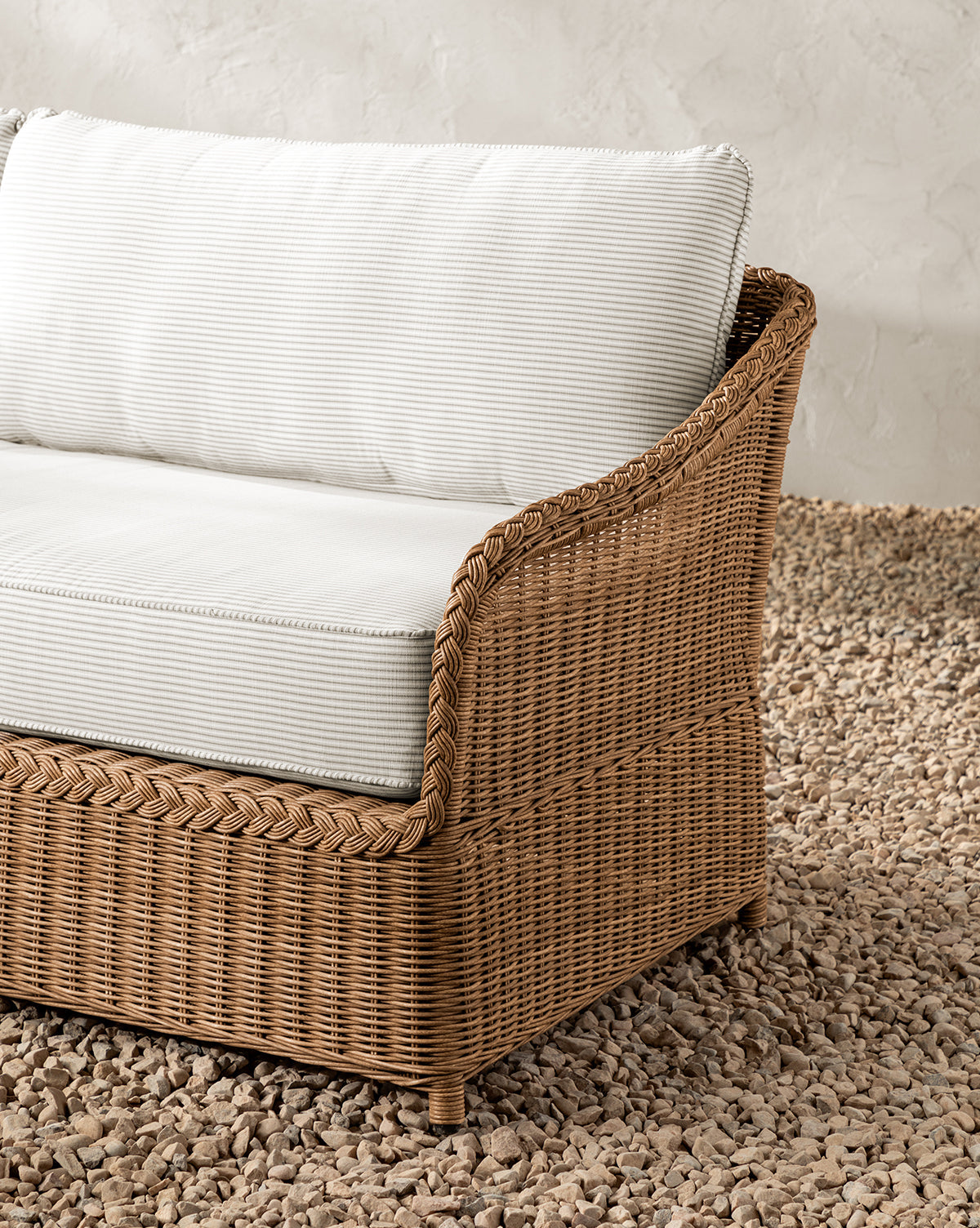 A close-up of the Haviland Outdoor Sofa with Perennials Taupe Stripe 88 and white cushions, set on a textured tan pebble floor against a light wall. The weather-resistant woven frame offers comfort and inviting style by McGee & Co.