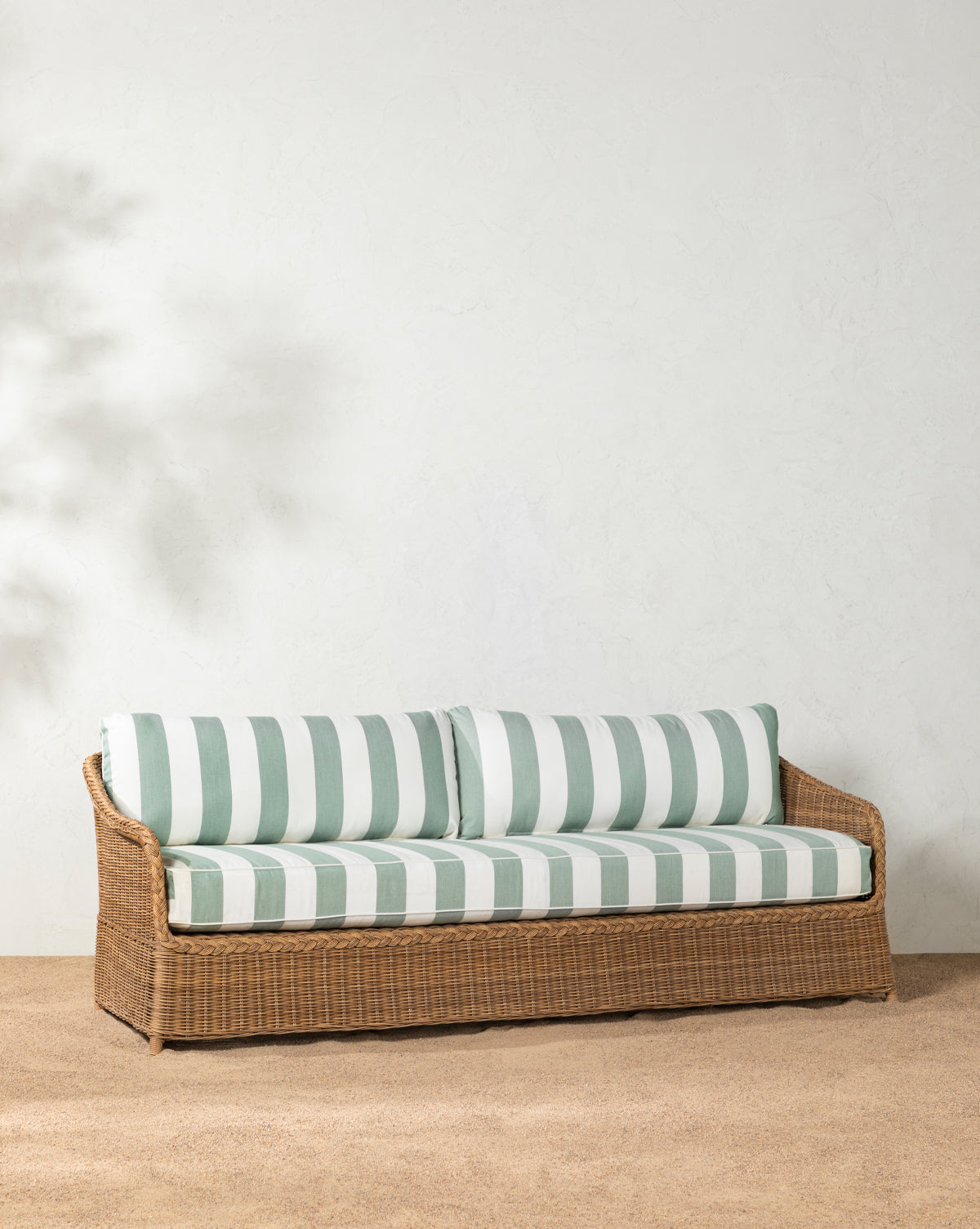 The Haviland Outdoor Sofa with Striped Cushions 88 sits on a textured beige rug against a white stucco wall for an inviting setup, with a small green plant visible on the right, by McGee & Co.