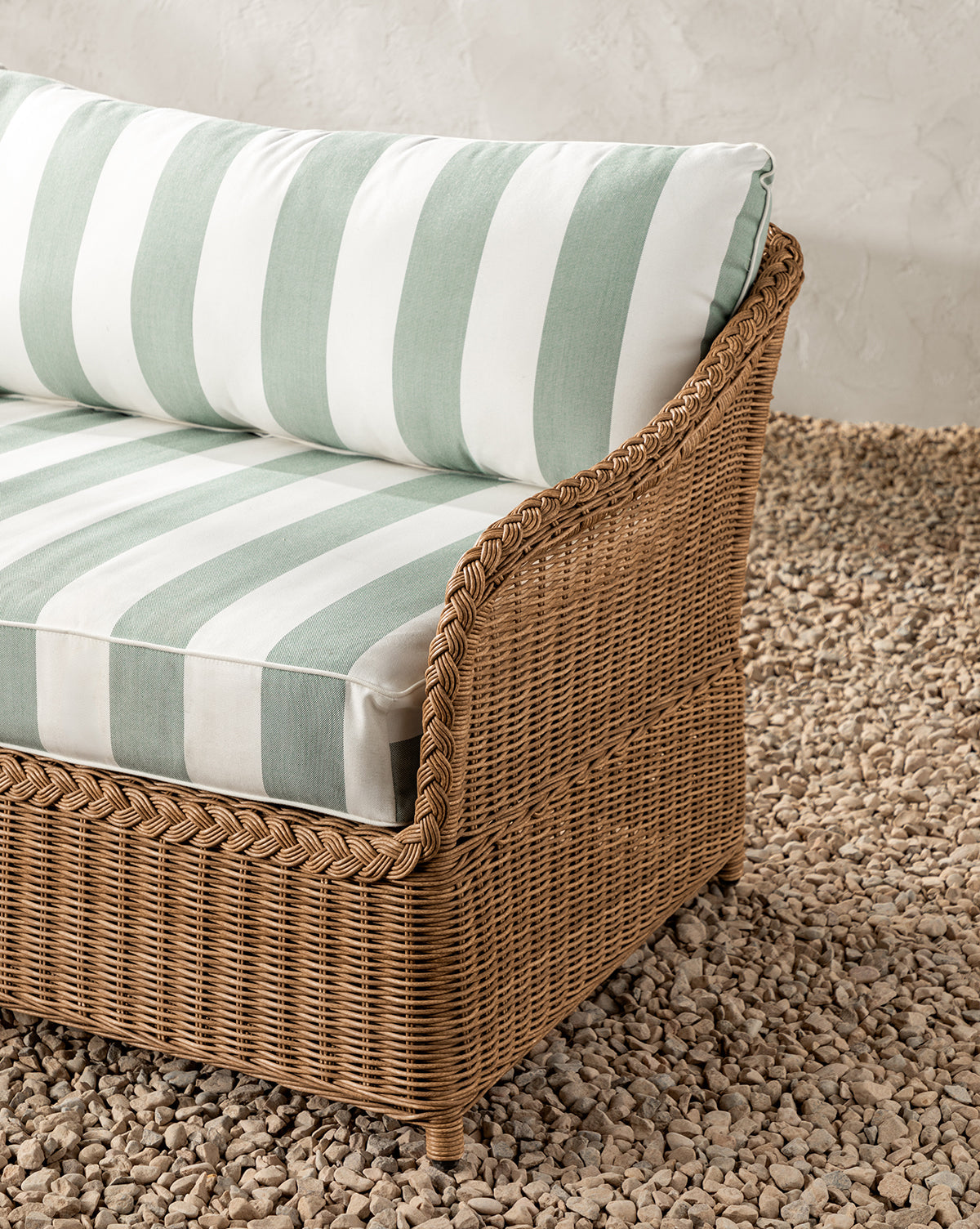 The Haviland Outdoor Sofa with Striped Cushions 88 features thick green and white striped cushions and rests on small light rocks before a neutral textured wall, bringing charm and comfort to any patio setting, by McGee & Co.